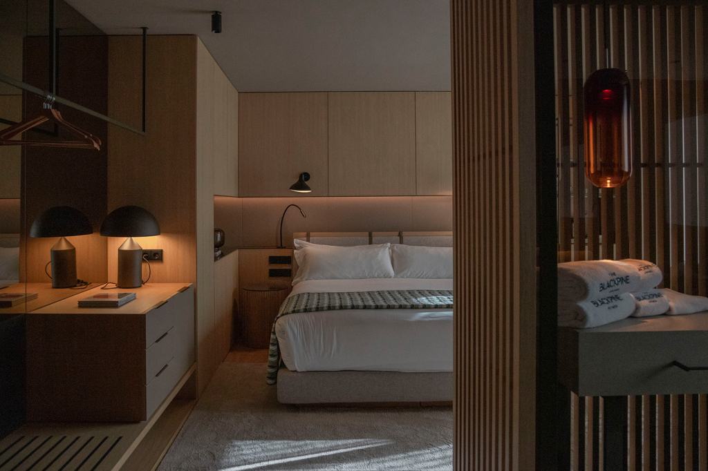 The Blackpine Hotel an SLH Hotel (Andorra) Room with dresser with table lamp with a ceiling-mounted hanging bar for clothes next to a bed with wall-mounted lighting