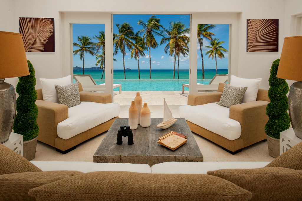 The Liming Bequia an SLH Hotel (Saint Vincent &amp; the Grenadines) Living Room with a couch and two lounge chairs with potted plants end tables and coffee table with a door to a private outdoor space with infinity pool and chaise pool chairs