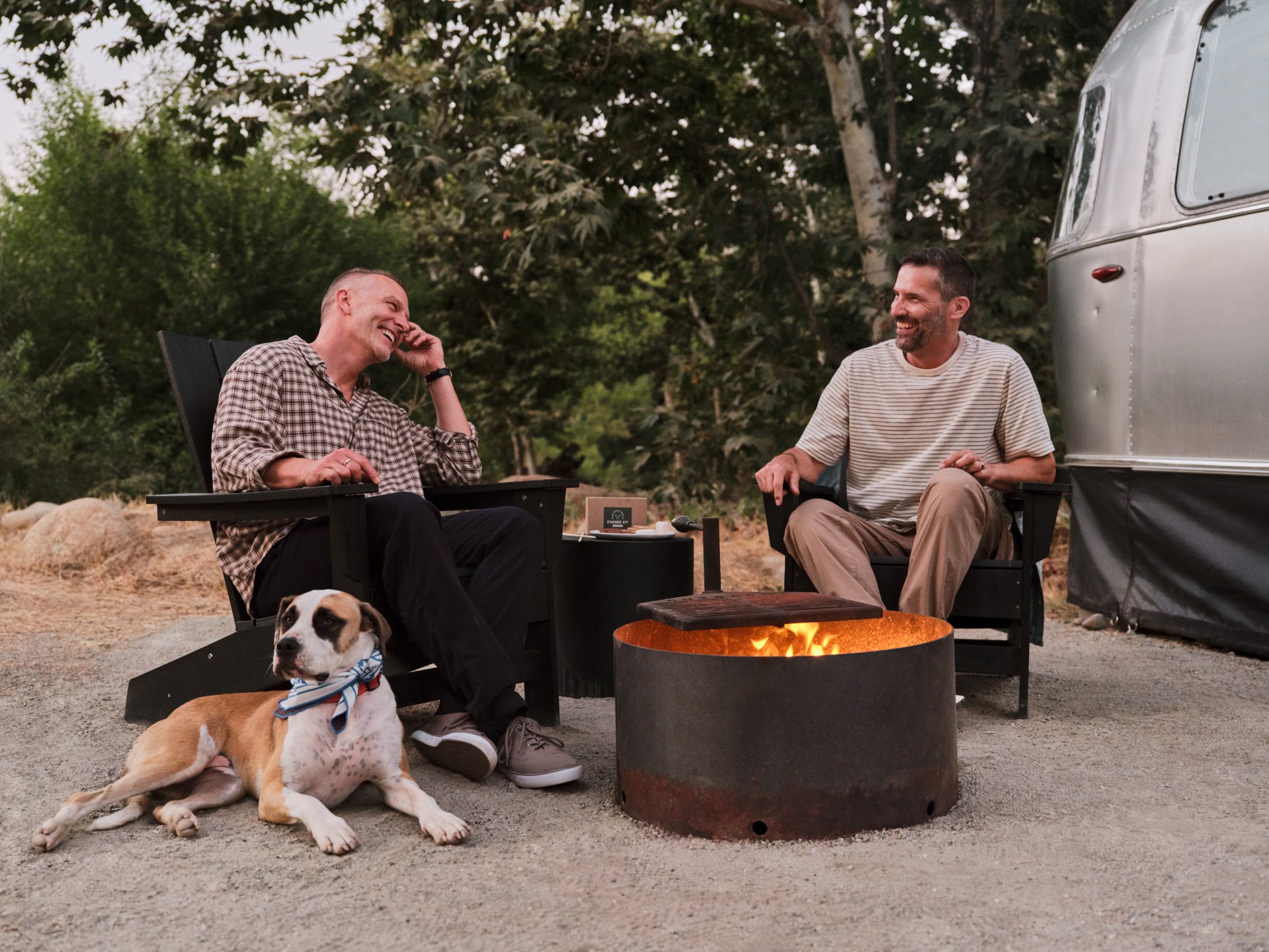 Two men and a dog sitting around a fire pit outside of AutoCamp Sequoia trailer