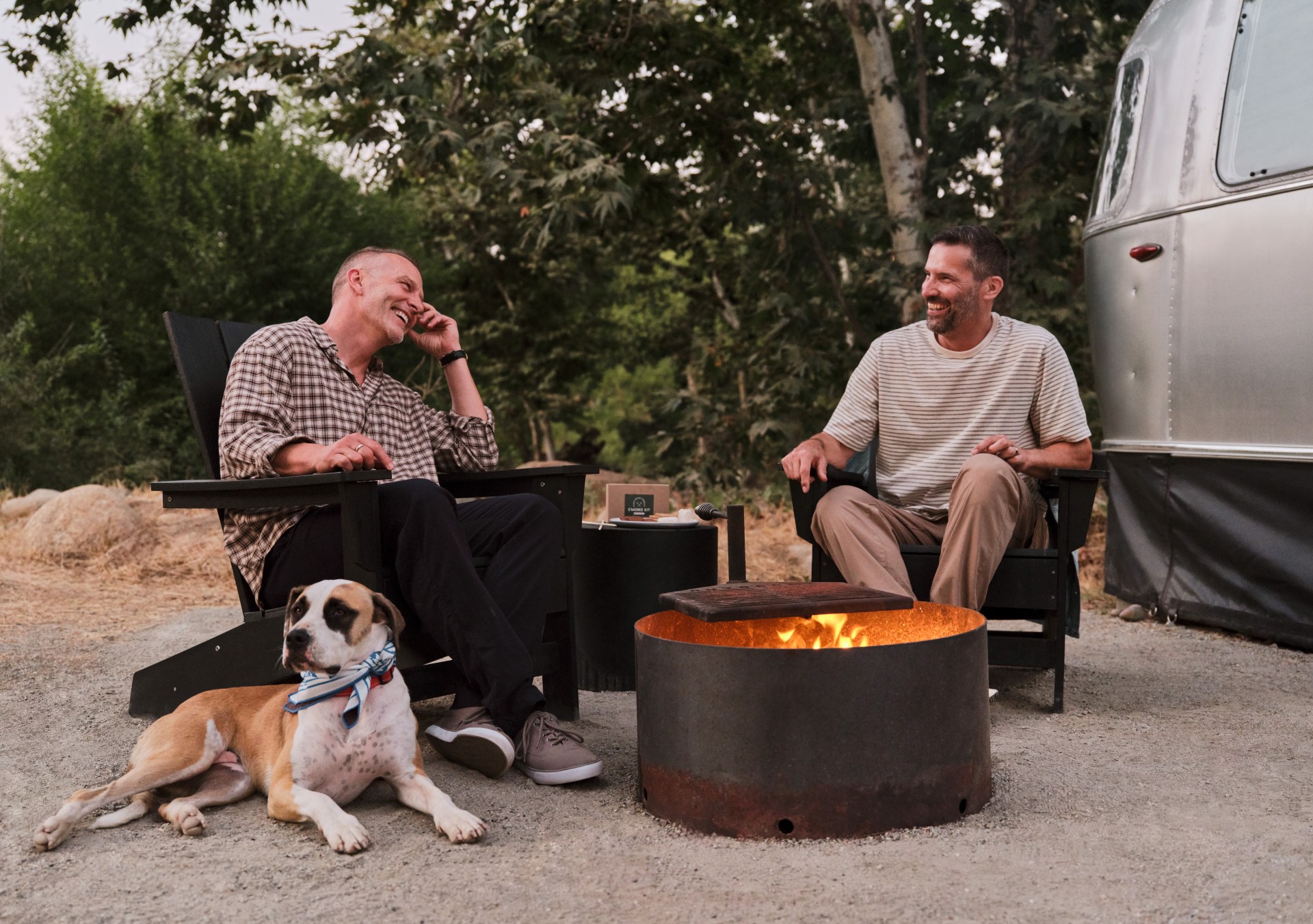 Two men and a dog sitting around a fire pit outside of AutoCamp Sequoia trailer