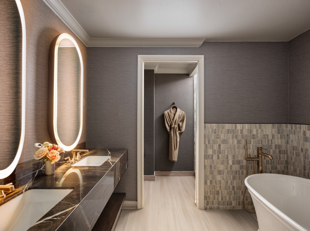 Suite bathroom with two sinks, a freestanding bathtub, and a robe hung on the wall