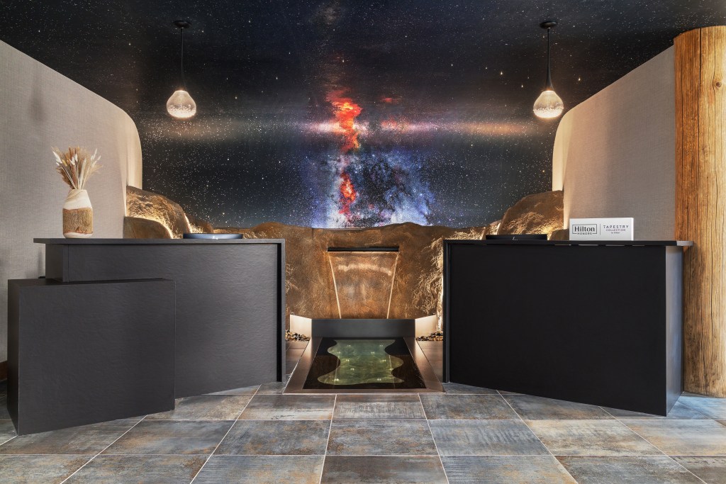 Lobby of Starlite Yellowstone, Tapestry Collection by Hilton with large night sky mural, rock feature, front desk area with two black desks