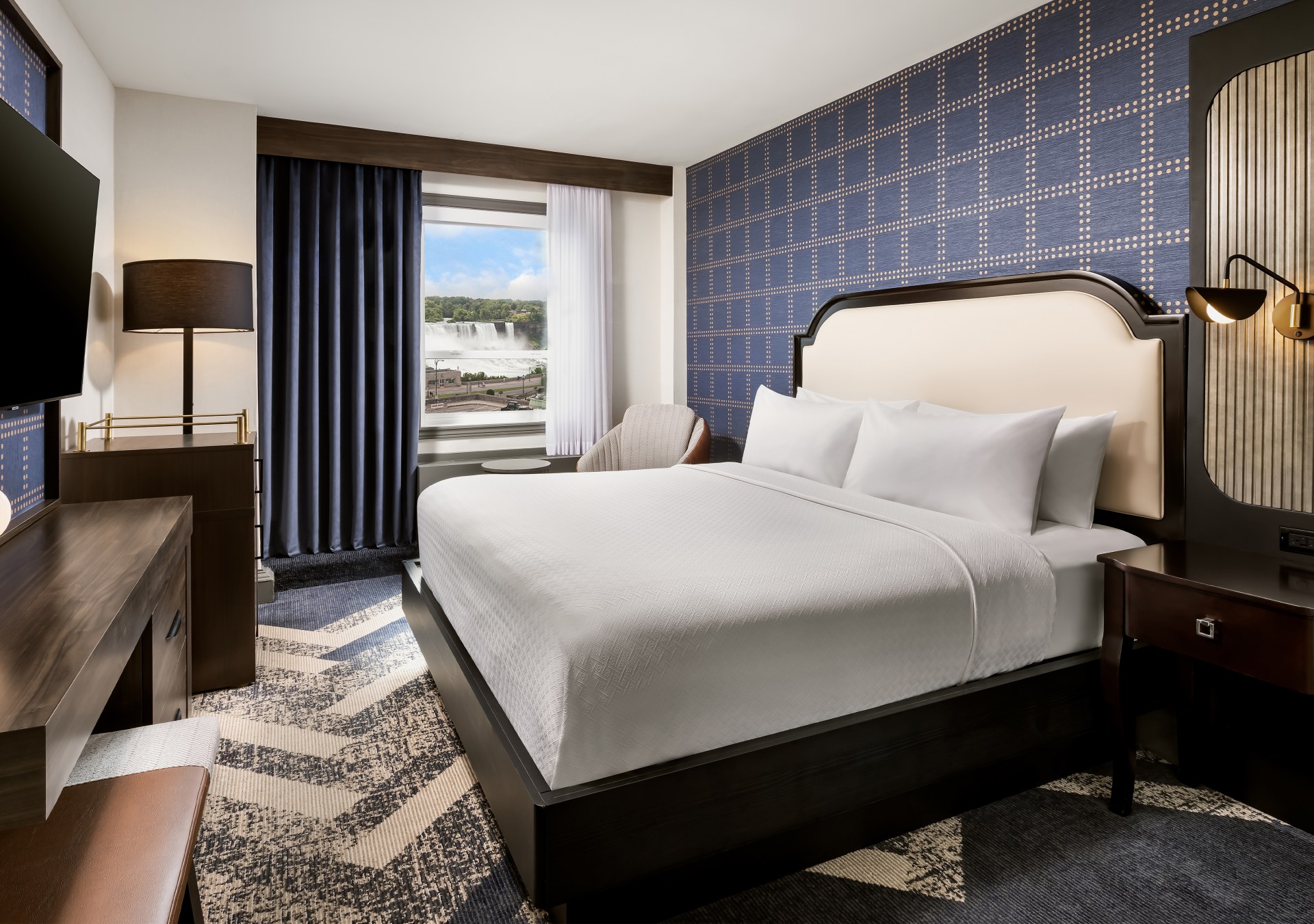 A bedroom with bed, tv, dresser, and chair.