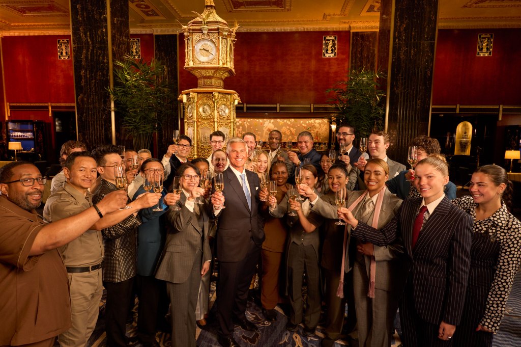 large group of Waldorf Astoria New York team members and Chris Nassetta, president and CEO, Hilton raise champagne glasses in Peacock Alley at Waldorf Astoria New York