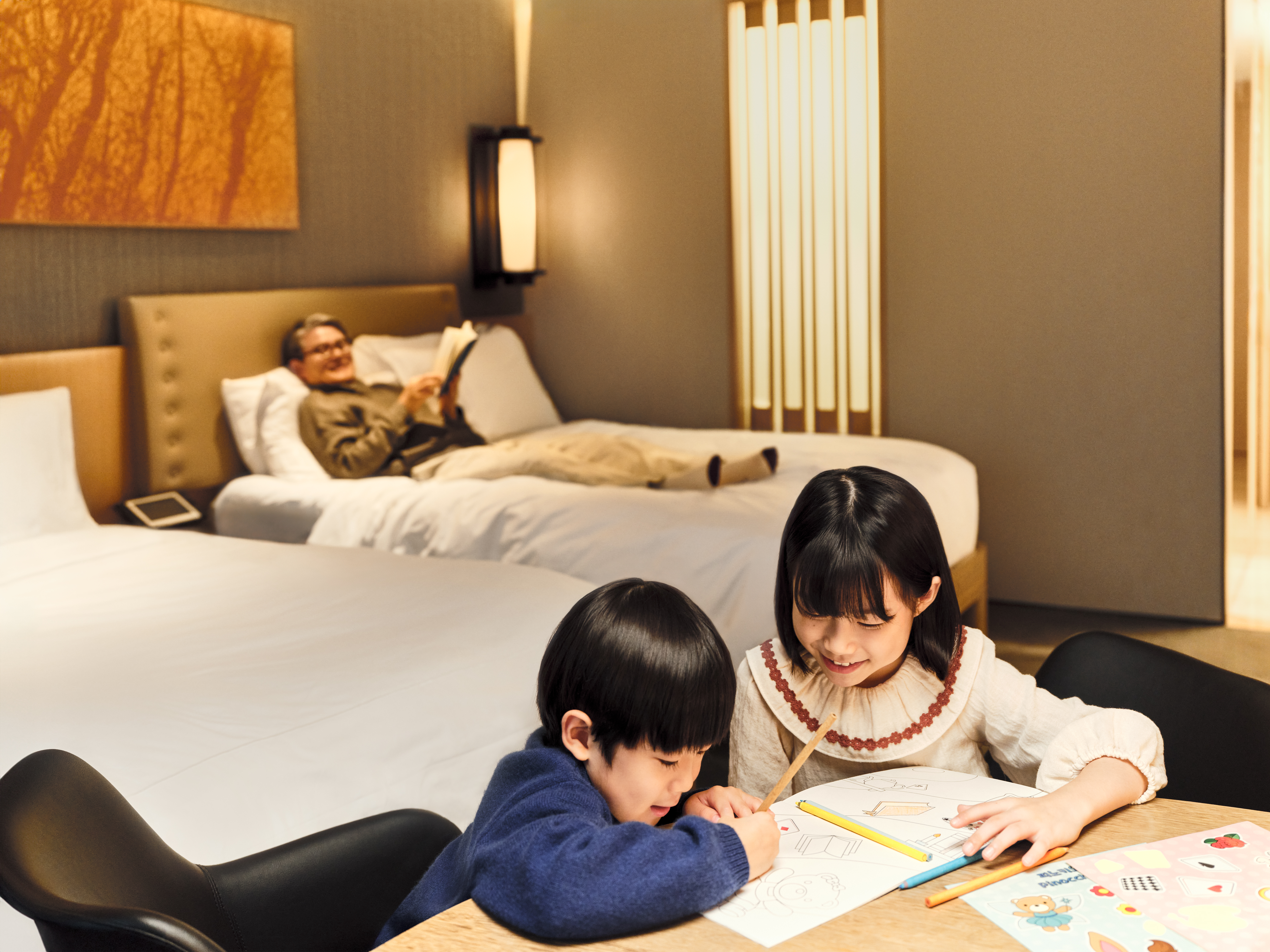 Conrad Seoul - Guest Room, kids coloring at desk while grandfather watches lounging with book on guest bed