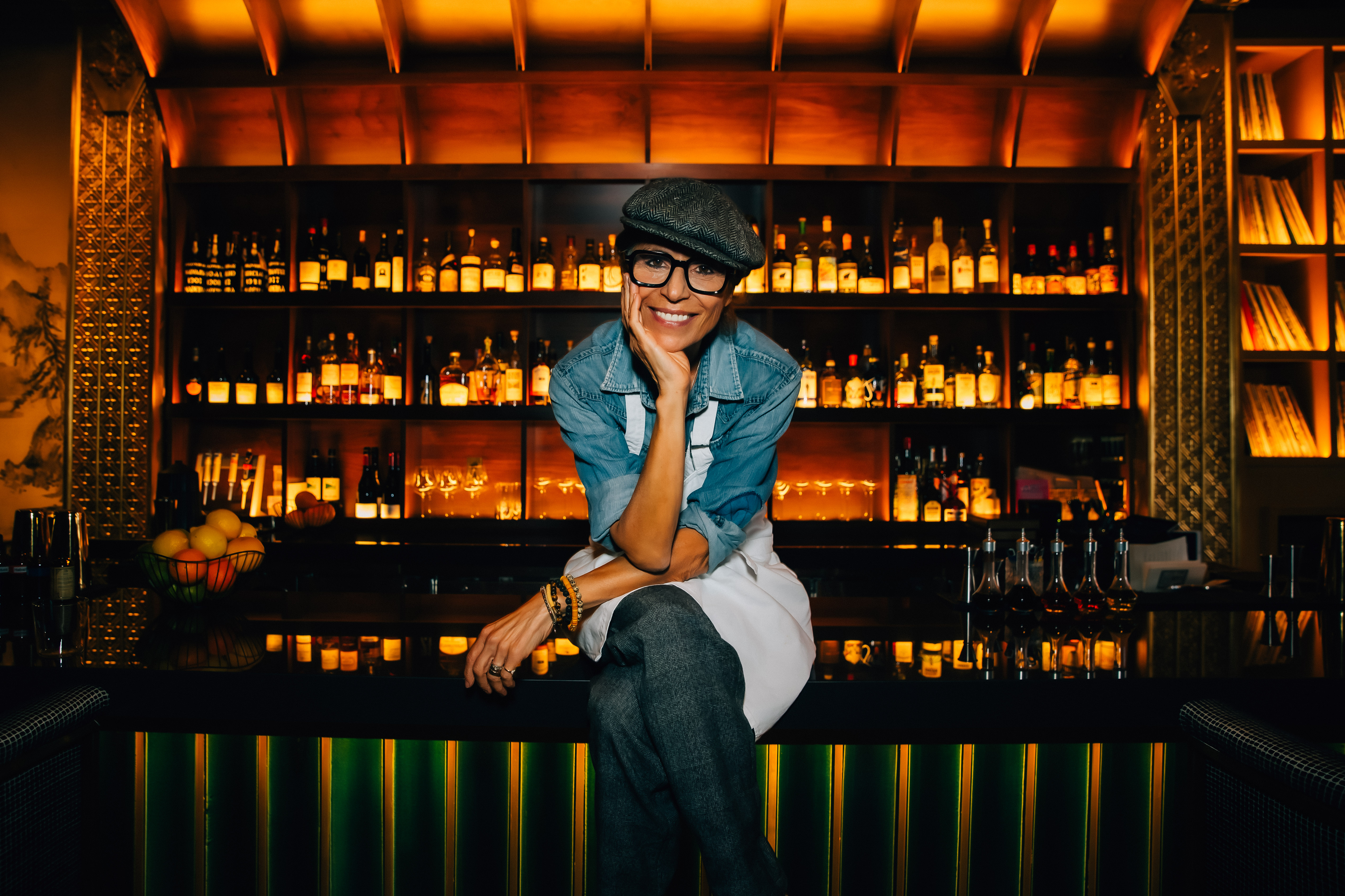 Dominique Crenn sitting in front of a bar, smiling at camera