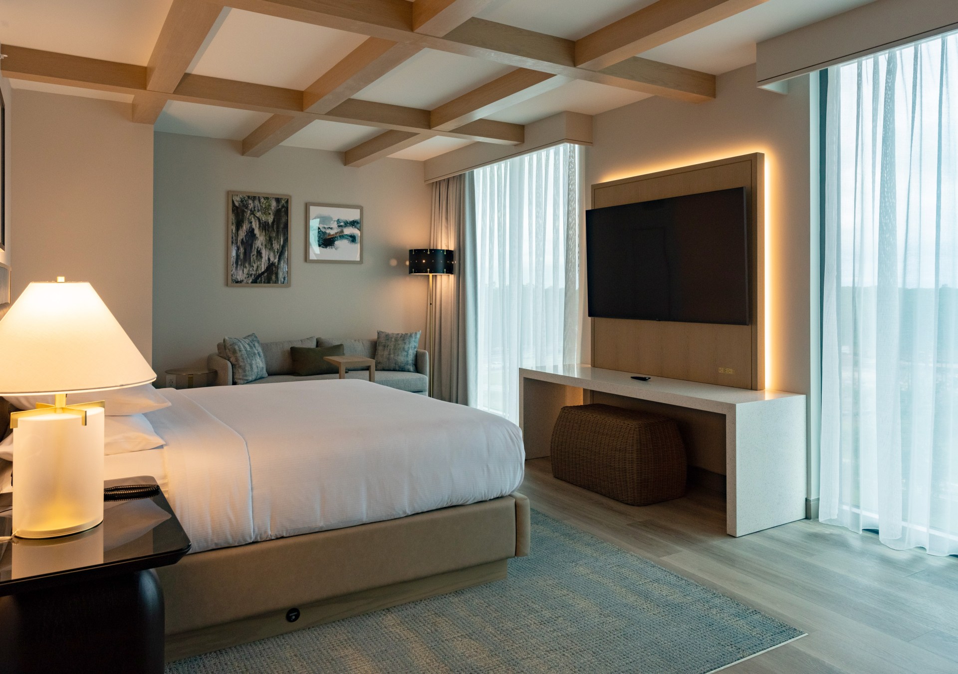 A room with bed, couch, tv, and large windows.