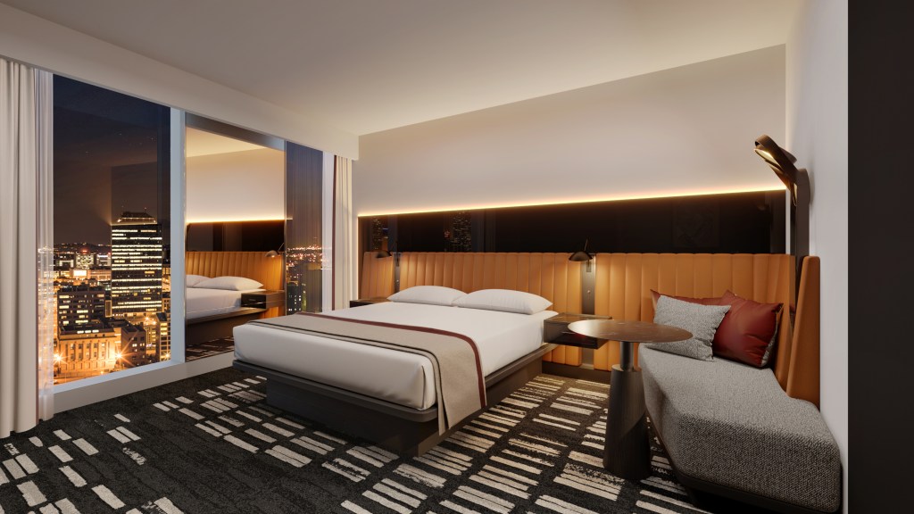 A king room with bed, chaise, and large window looking out on the city lights