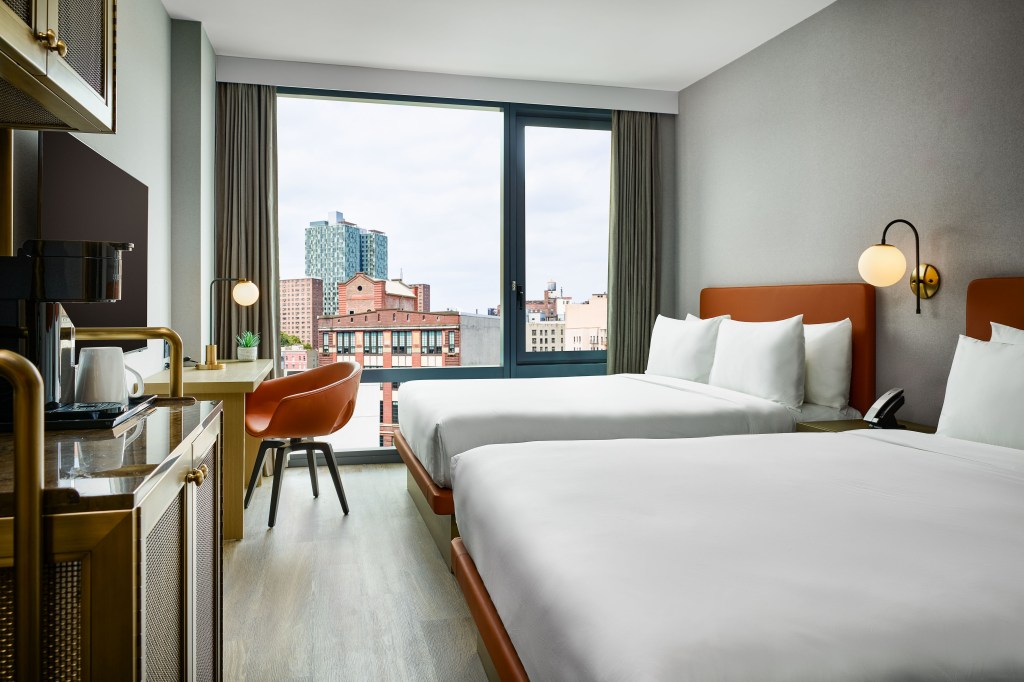 A bedroom with 2 queen bed, desk, tv, coffee bar, and window overlooking the city.