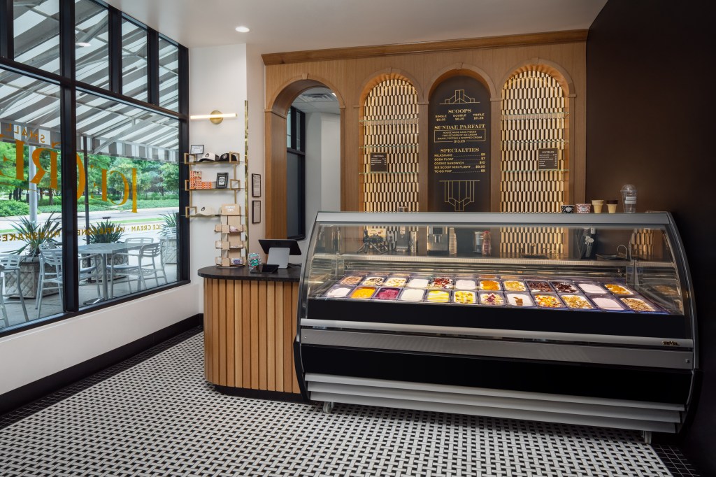 An ice cream shop with ice cream case, and windows looking over outdoor tables