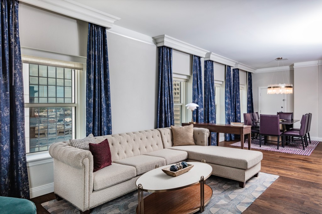 A room with couch with chaise, and dining table in background