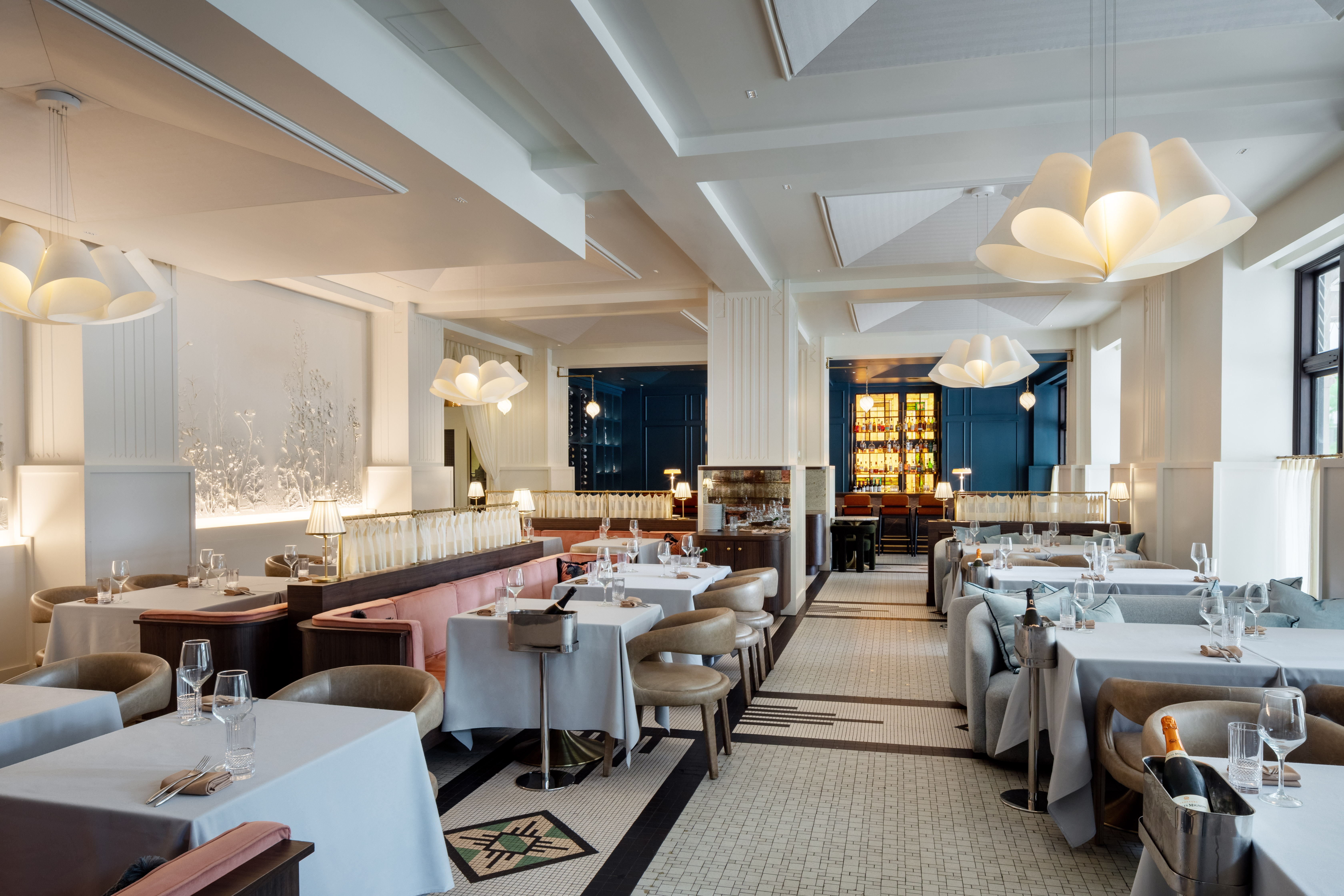 An elegant dining room with various couches and chairs at tables with table cloths and ice buckets for wine.