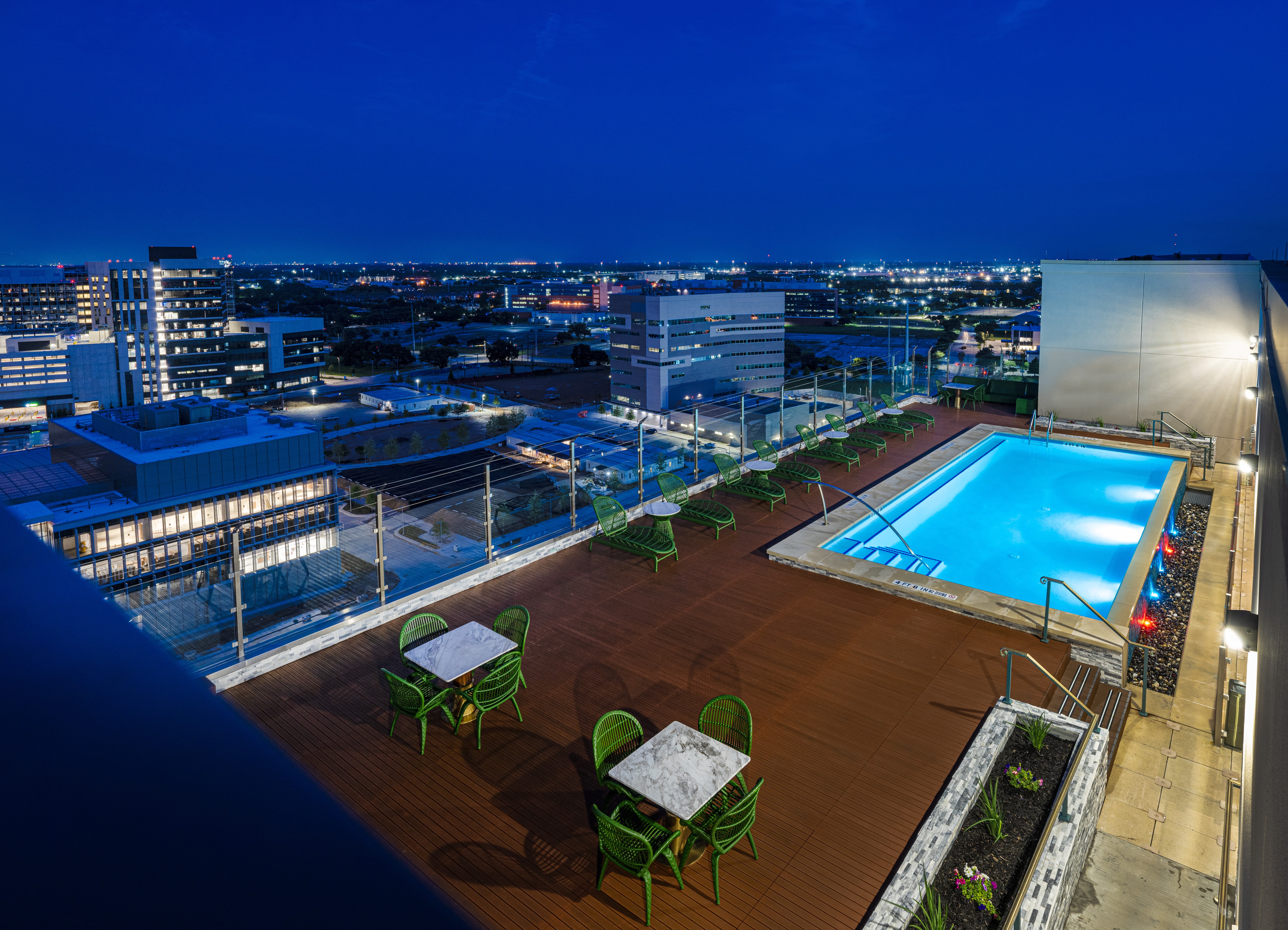 The rooftop pool at night surrounded by lounge chairs and looking out over the city