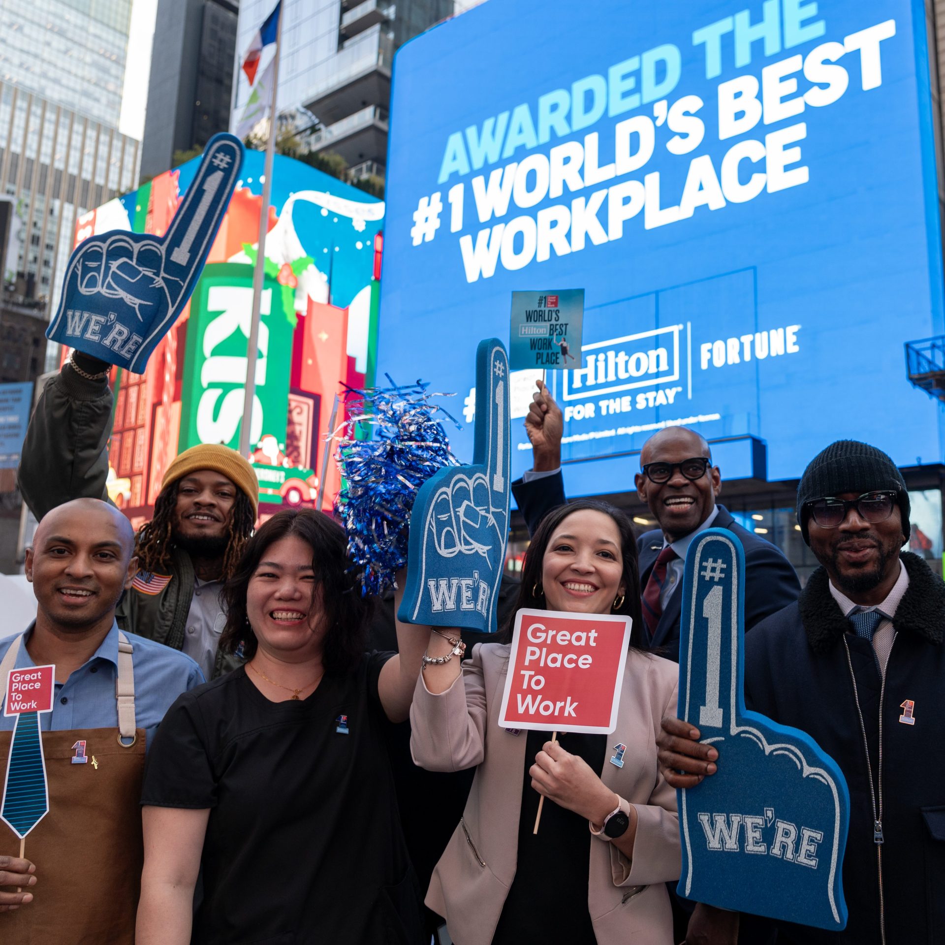 Group holding signs in front of Hilton #1 World's Best Work Place Screen in Times Square