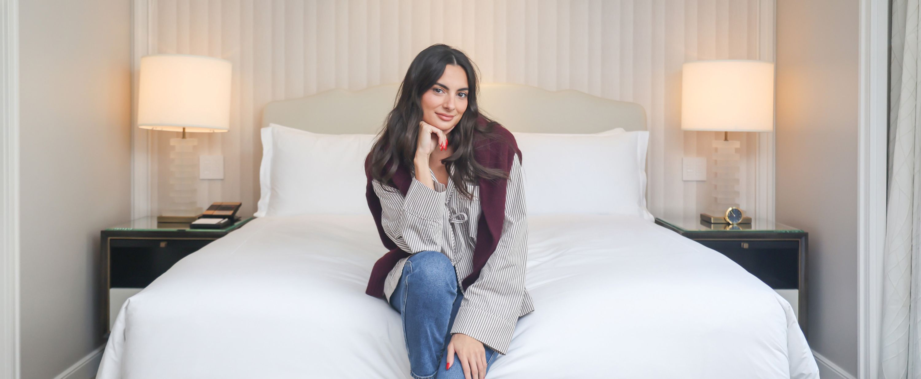 Paige DeSorbo sits on the end of the bed, smiling at camera
