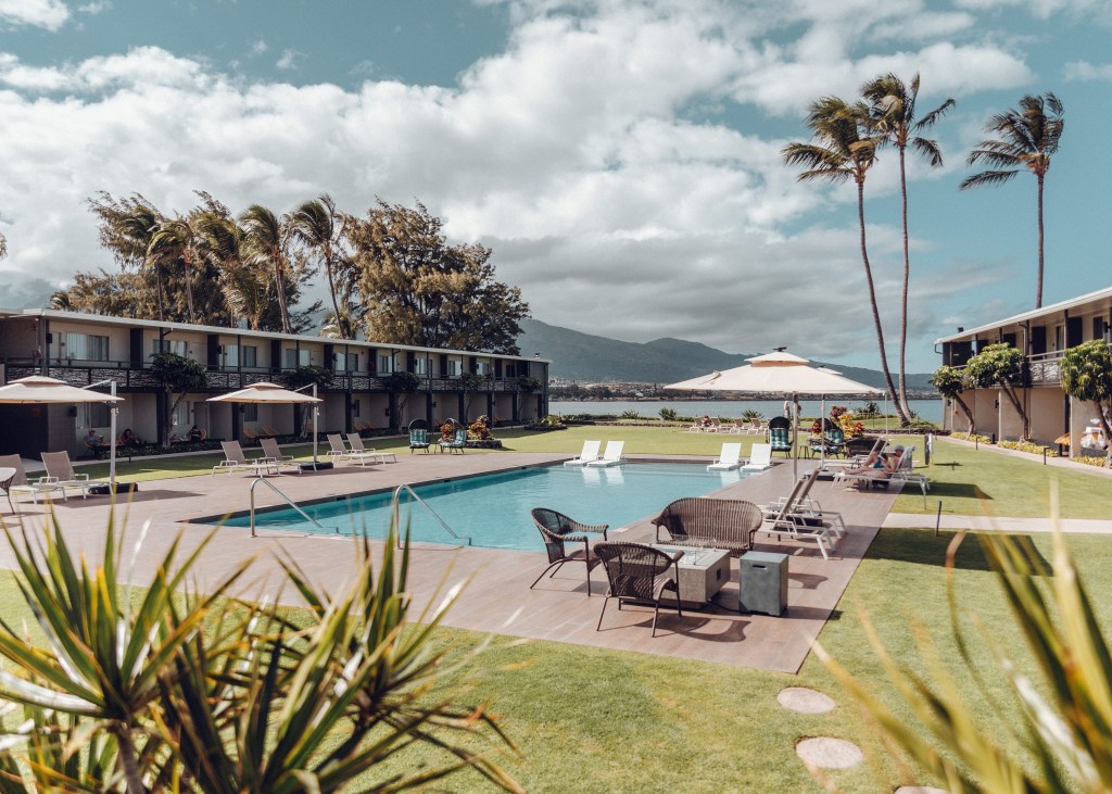 Pool with lounge chairs and umbrellas looking out at the view at the Maui Seaside Hotel