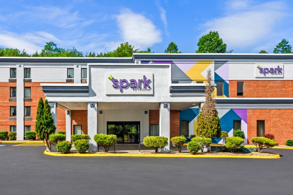 Spark by Hilton Lexington exterior entrance with green landscaping around the drop-off zone, brick exterior of building, colorful painting on side of building