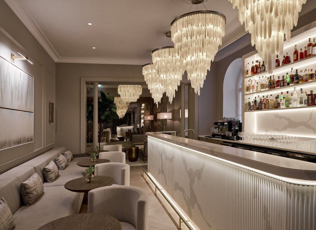 Elegant hotel bar with chandeliers and marble counter.
