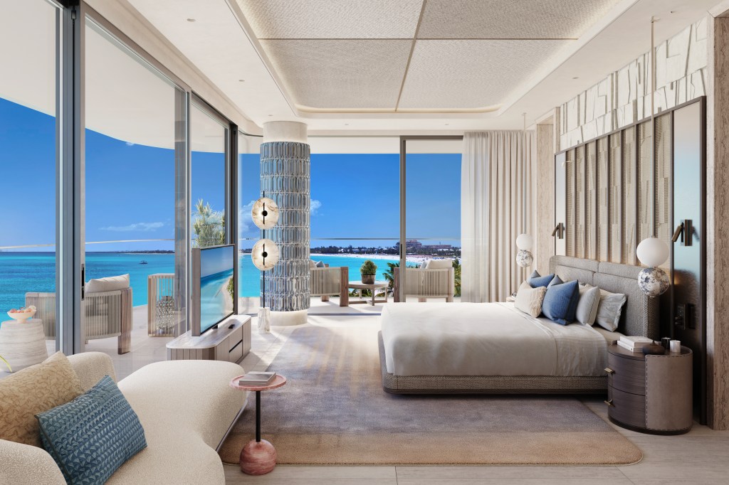 A room with bed and chaise in front of floor to ceiling windows looking at the balcony and ocean beyond