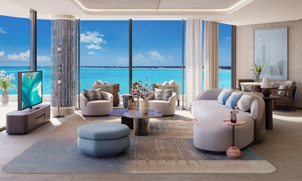 A living room with couch, chairs, table, tv, and large floor to ceiling windows looking out at the ocean.