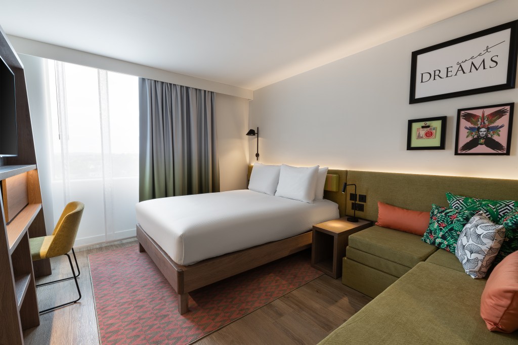 Hampton by Hilton Stuttgart Airport - guest room with white bed, green seating area, colorful artwork