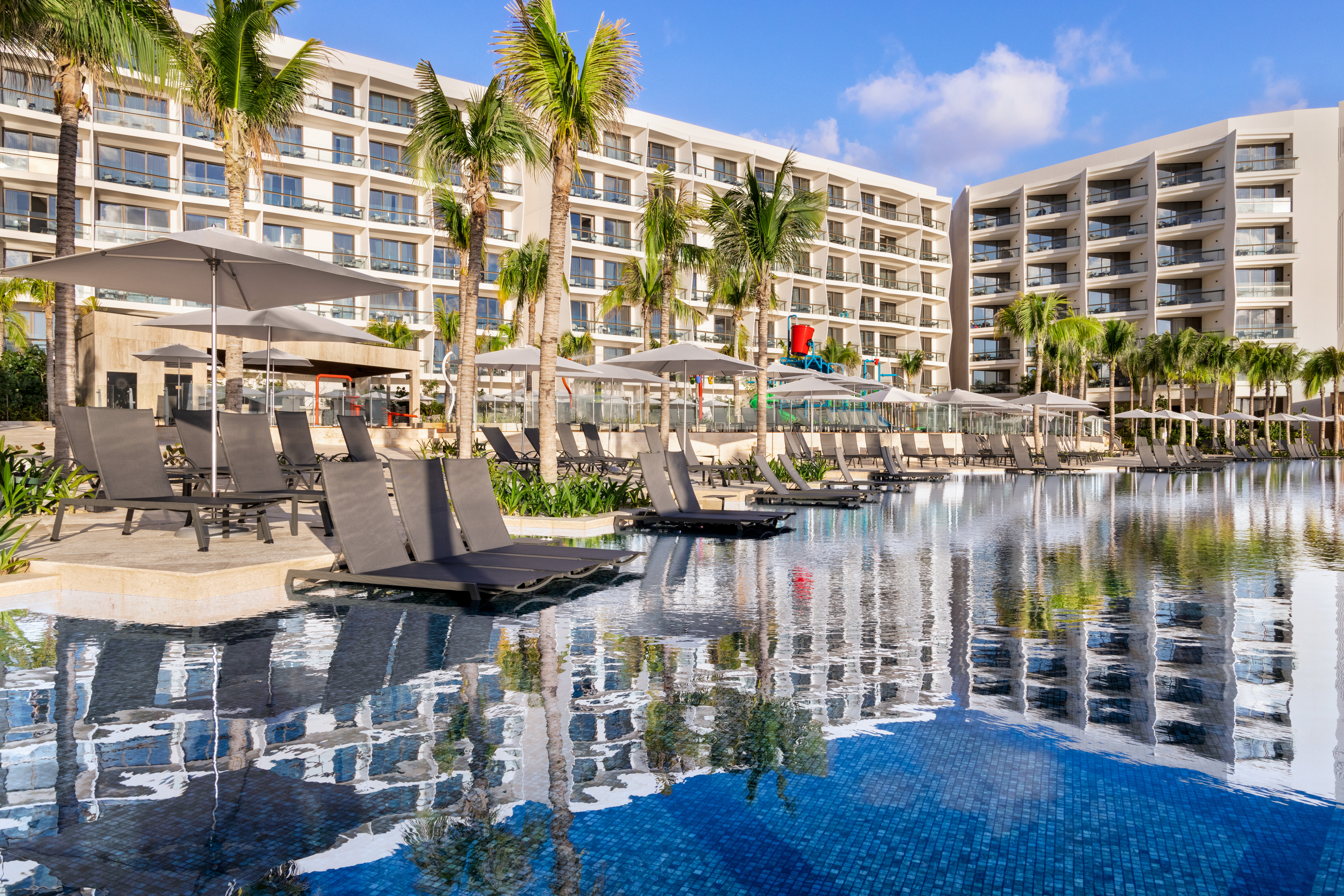 Lounge chairs and umbrellas in and around the pool with the hotel in the background