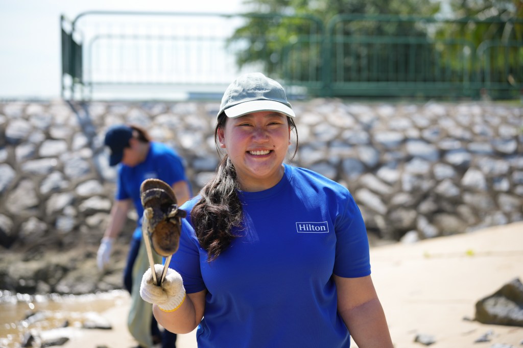 Hilton Travel with Purpose Week 2025 - Singapore Corporate Office - team member smiling while cleaning seashore