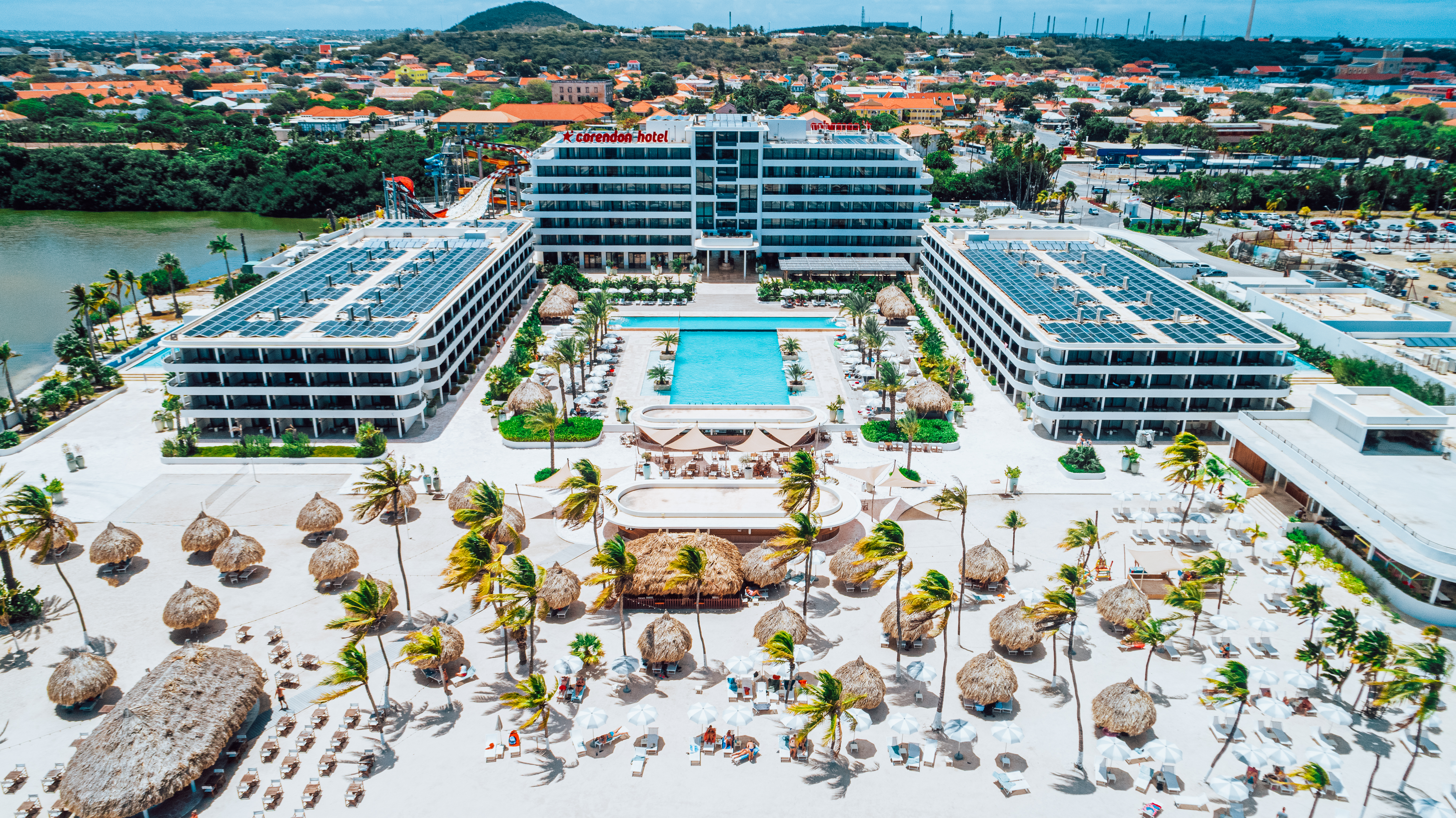 an aerial shot of the hotel, pool, with beach filled with lounge chairs and cabanas in front.