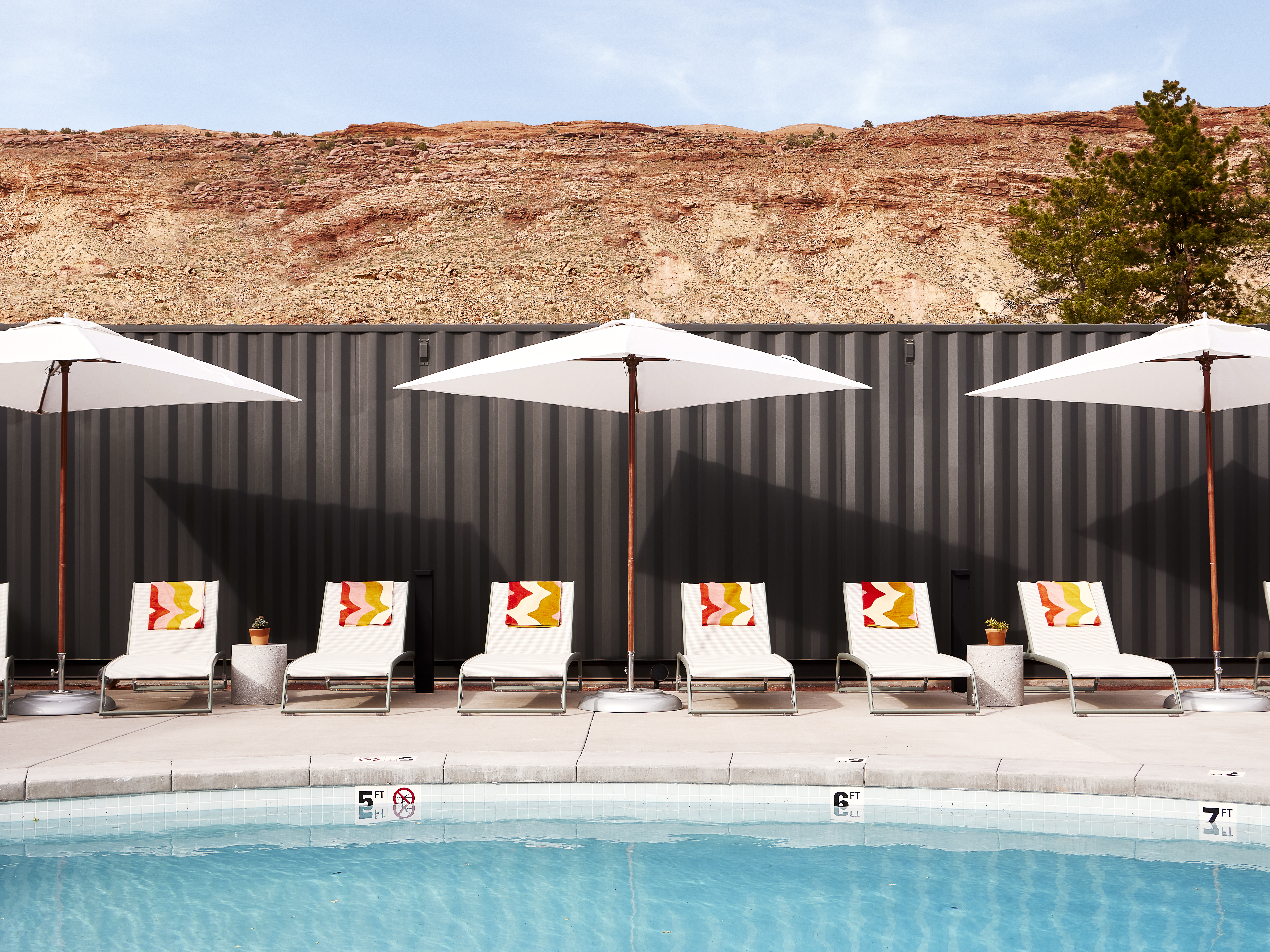 The edge of the pool, with lounge chairs, umbrella, and mountains in the background