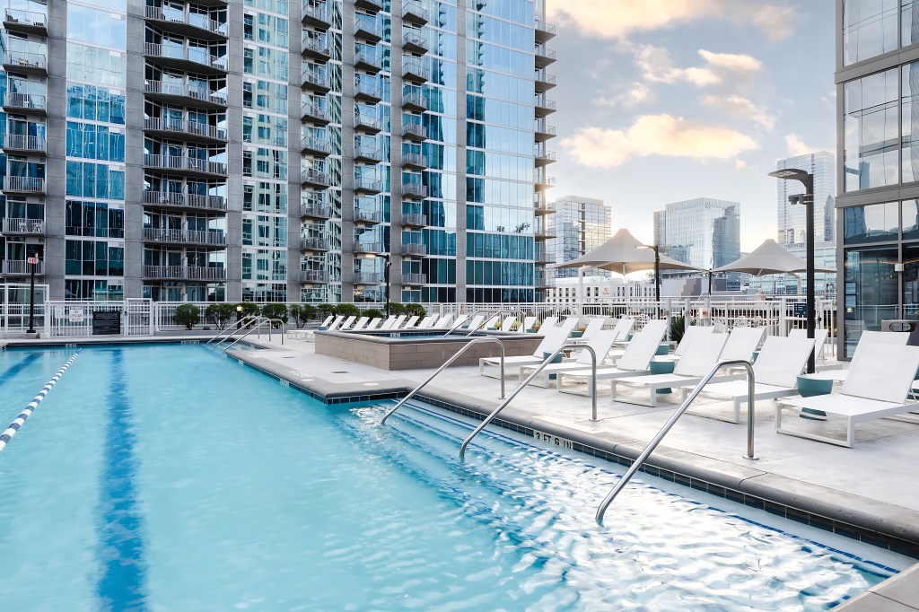 Rooftop pool with white chaise lounge seating and umbrellas overlooking the city.