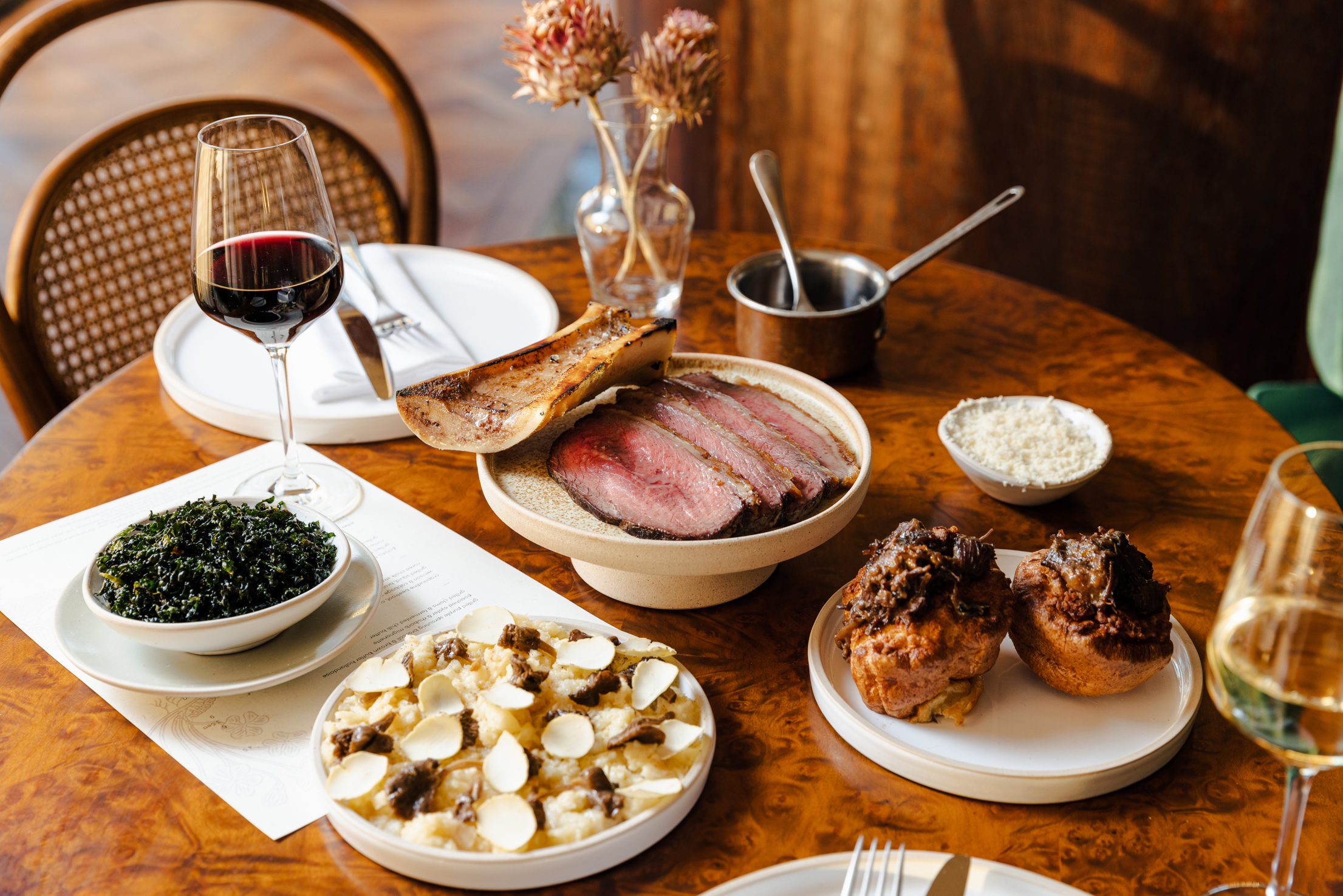 Plated food and stemmed glassware with red wine and white wine with flowers in a clear glass vase