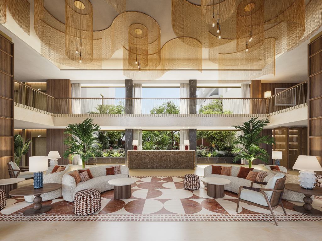 Modern lobby with high ceilings, golden mesh light fixtures, curved sofas, patterned rug, plants, and central reception in a warm, elegant setting.