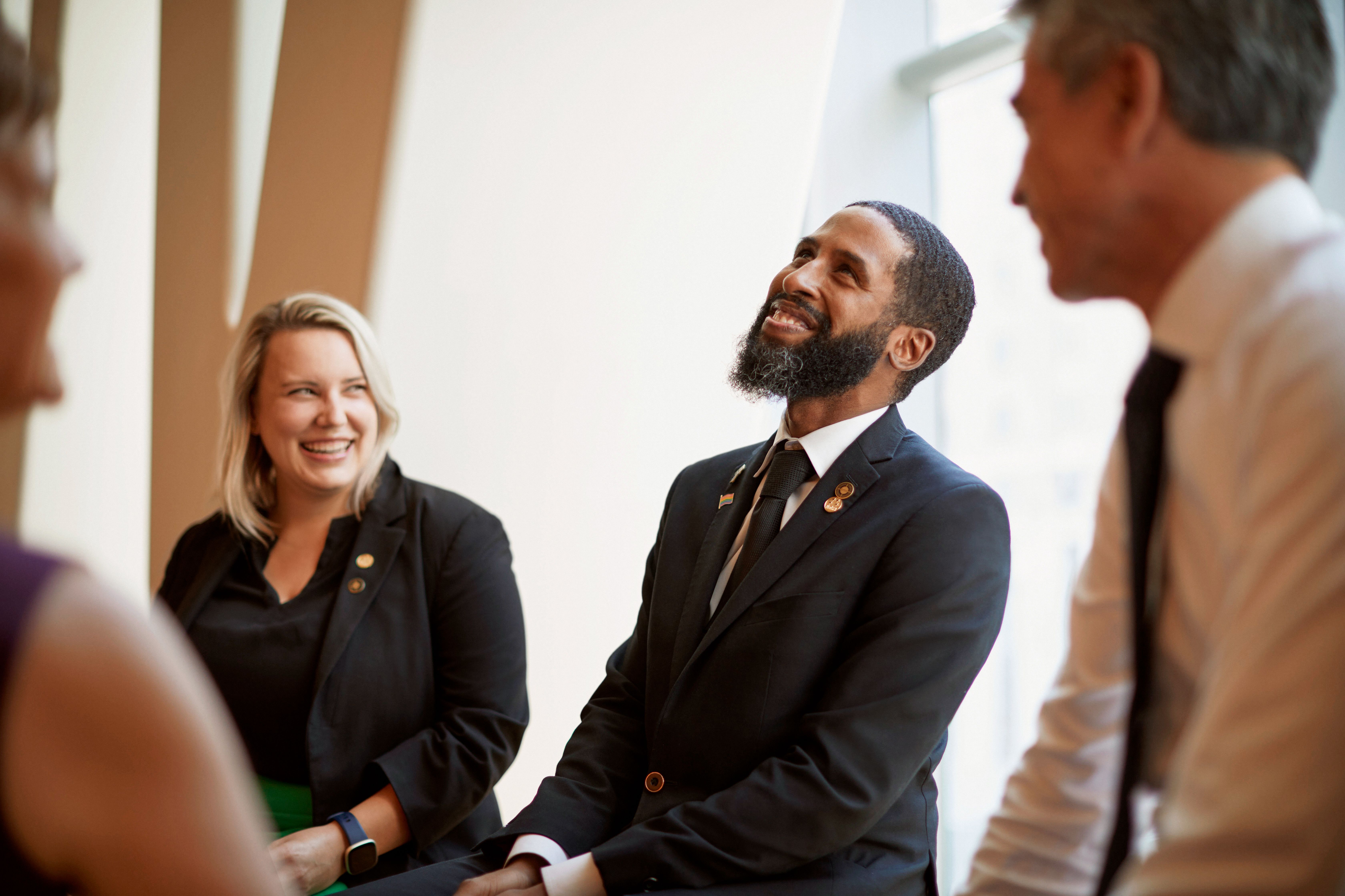 Four professionals wearing business attire smiling and engaging in conversation in a bright office setting.