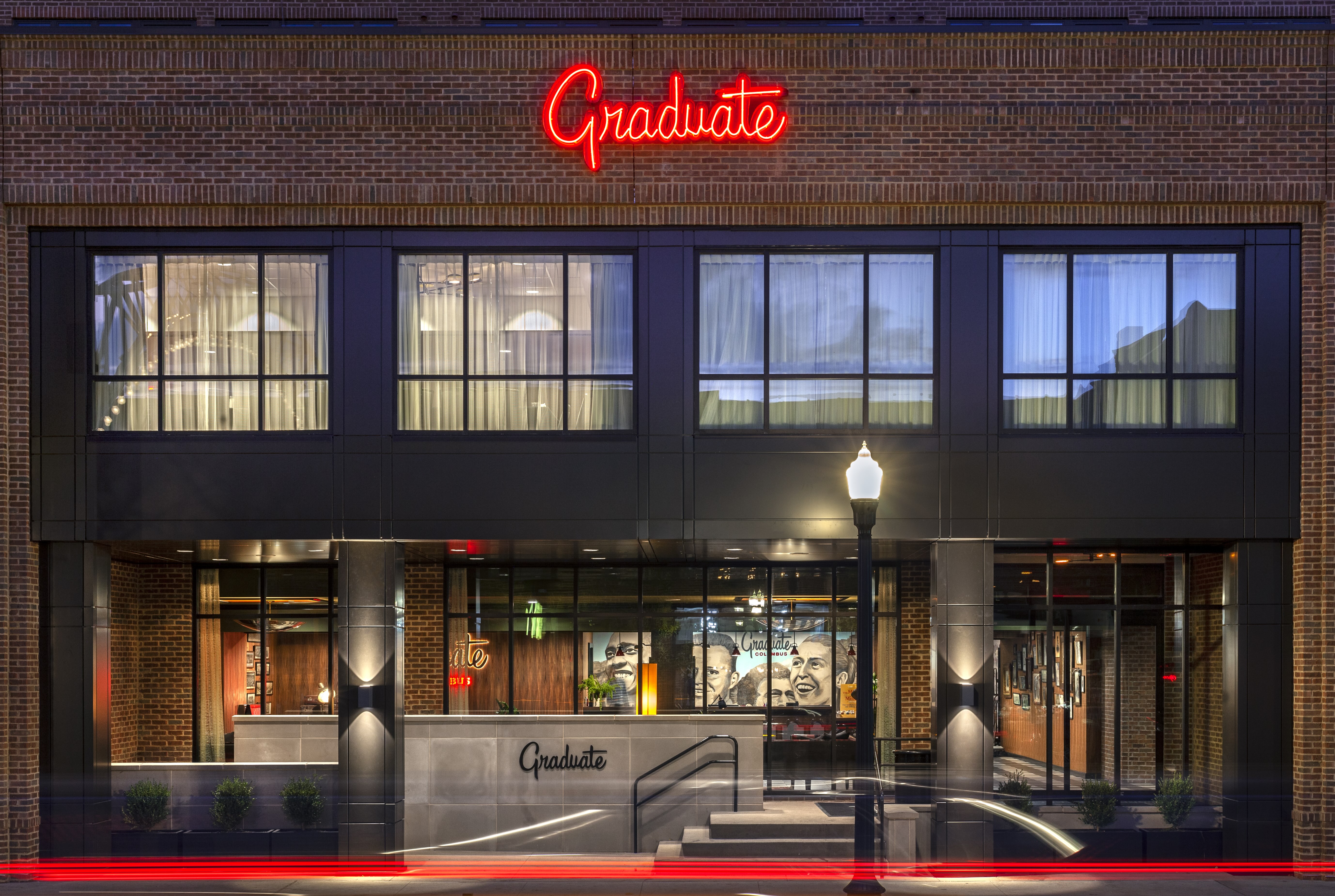 Brick building facade with large windows and a red neon "Graduate" sign above the entrance, illuminated at night.