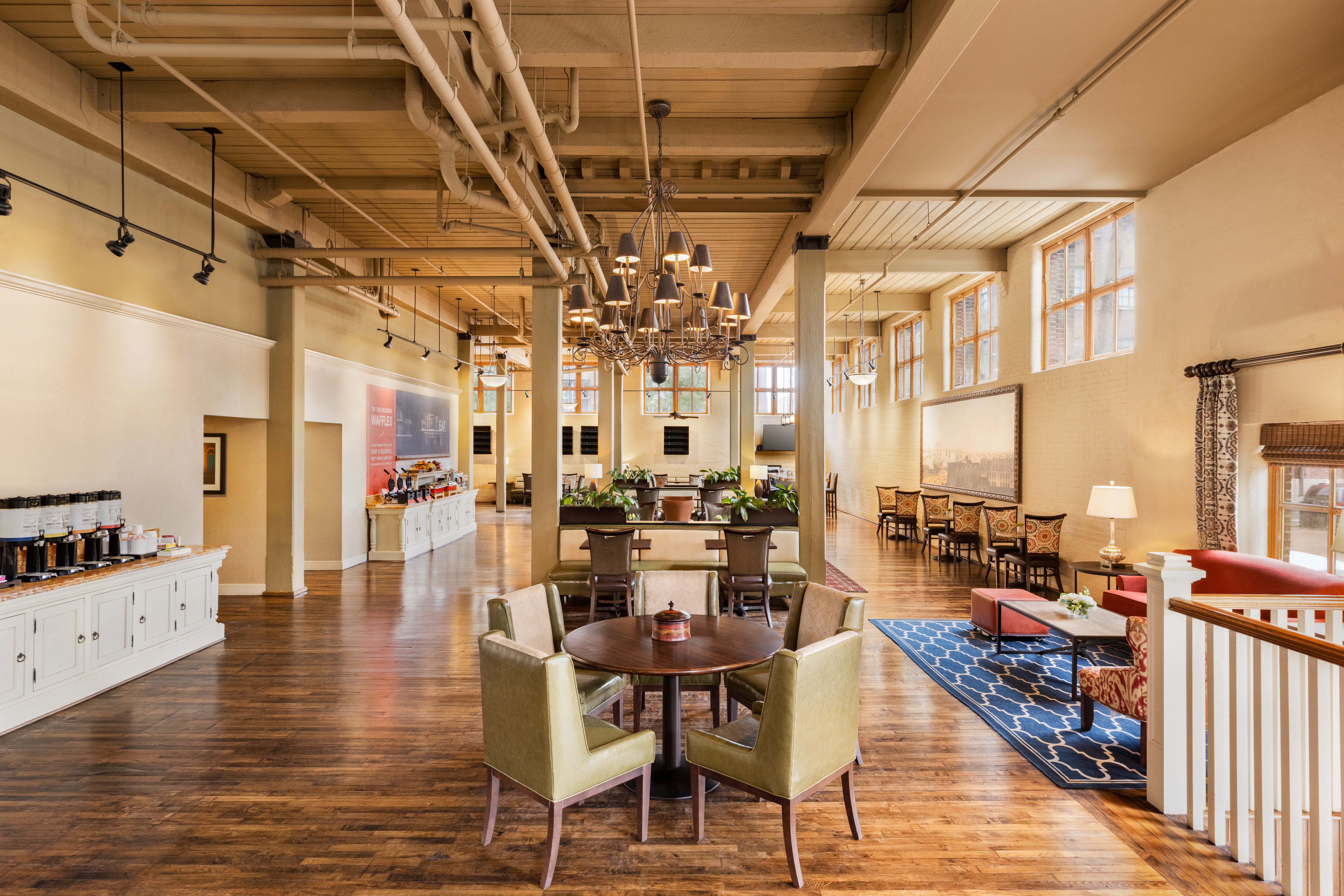 Spacious dining area with wooden floors, chairs around a round table, a chandelier, and large windows letting in natural light.