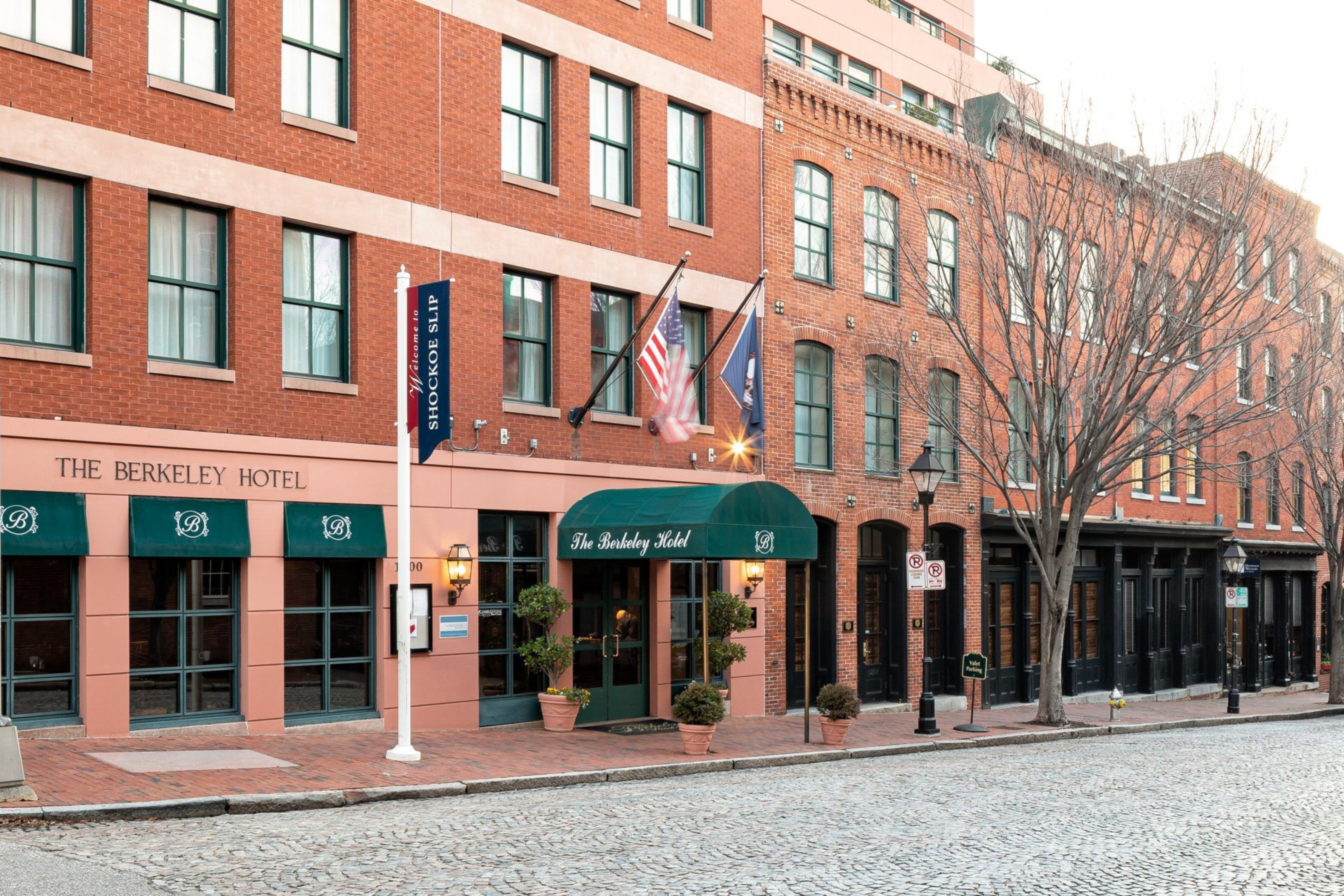 Brick building with green awnings and flags outside The Berkeley Hotel on a cobblestone street.