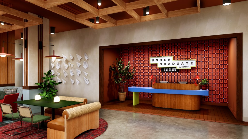 Modern hotel lobby with a colorful reception desk, patterned red wall, and seating area featuring green and tan chairs.