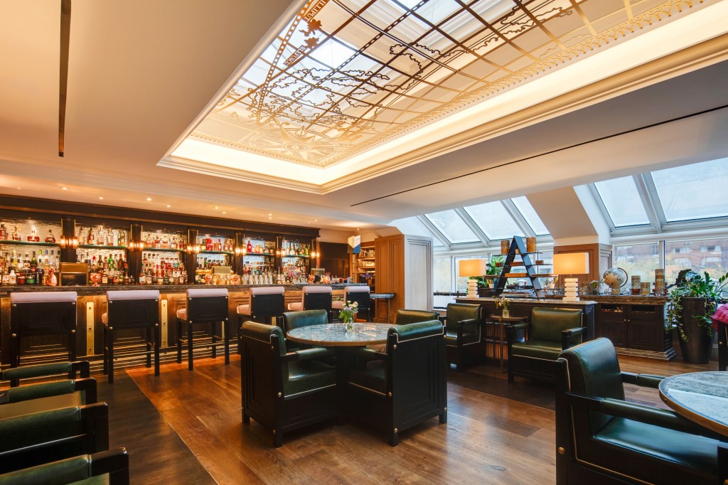 Upscale bar interior with dark wood furniture, leather chairs, a marble table, and a backlit ceiling panel featuring a decorative map design at Conrad Dublin.