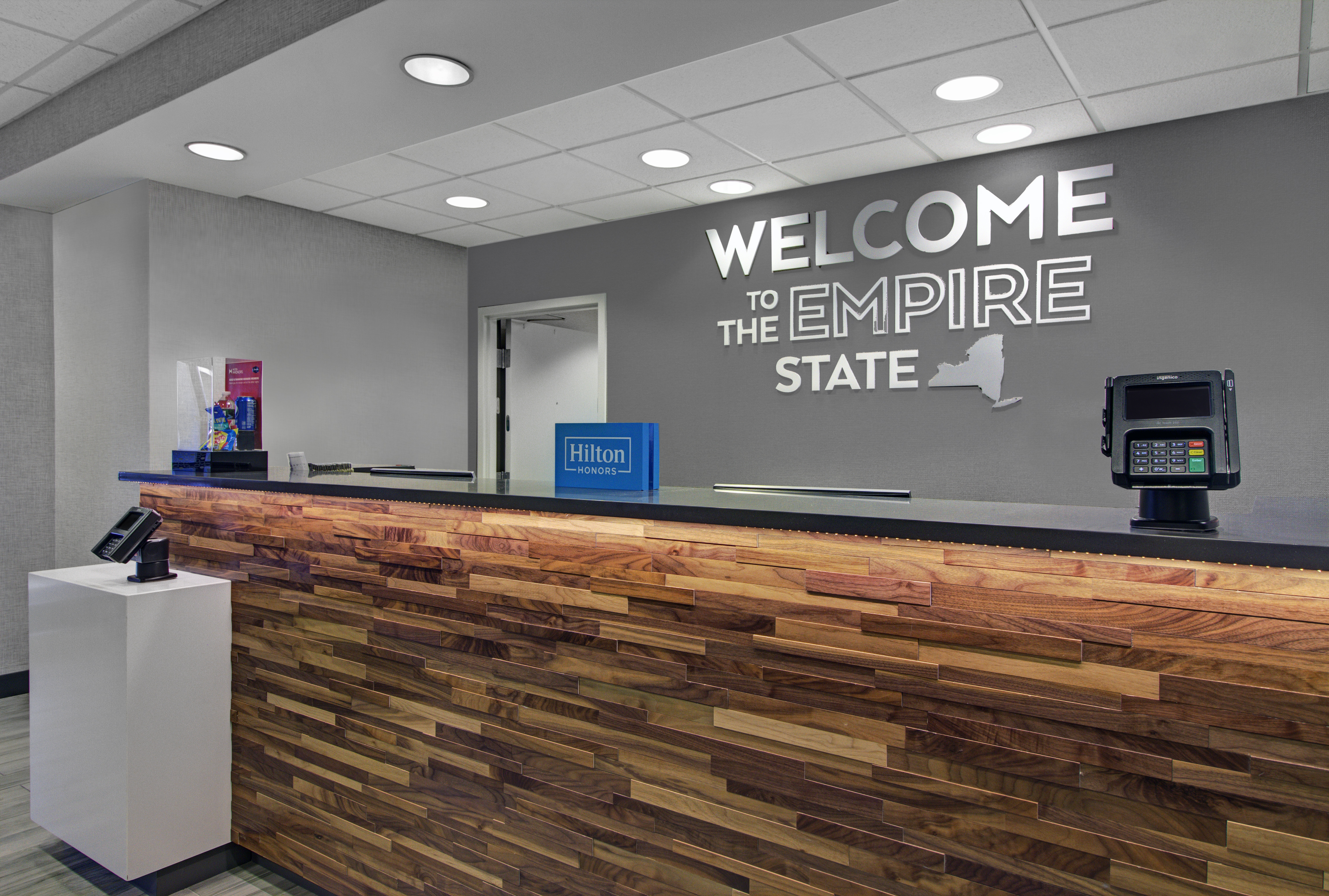 Hotel reception desk with a wooden front panel and a sign on the wall reading "Welcome to the Empire State."