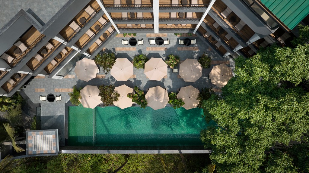 Aerial view of a rectangular swimming pool surrounded by umbrellas, lounge chairs, and greenery in a modern hotel courtyard at the Spark by Hilton Goa Calangute.