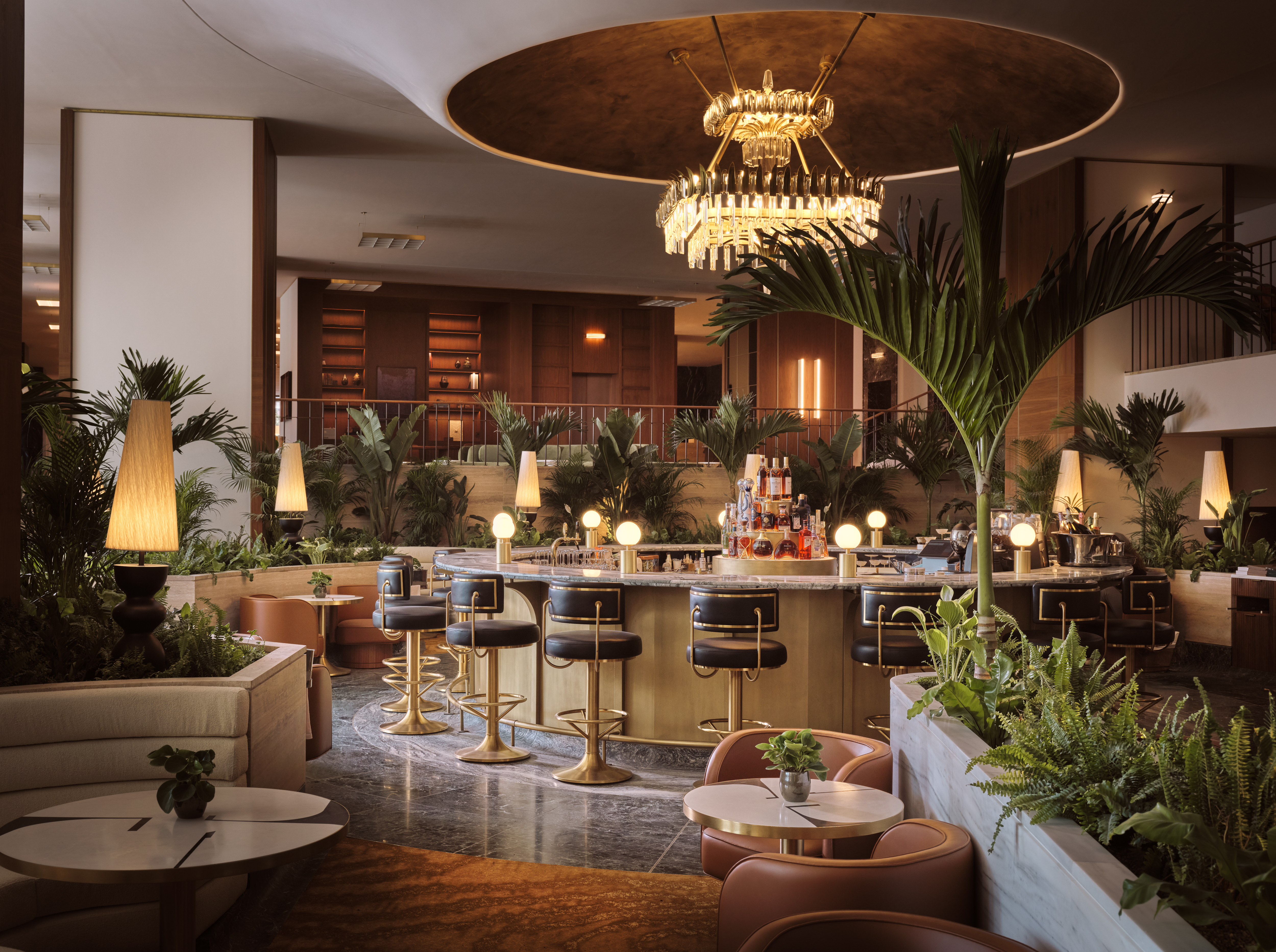 Luxurious Conrad Athens The Ilisian Athenian Lounge with a circular marble counter, black and gold bar stools, warm lighting, and abundant green plants.