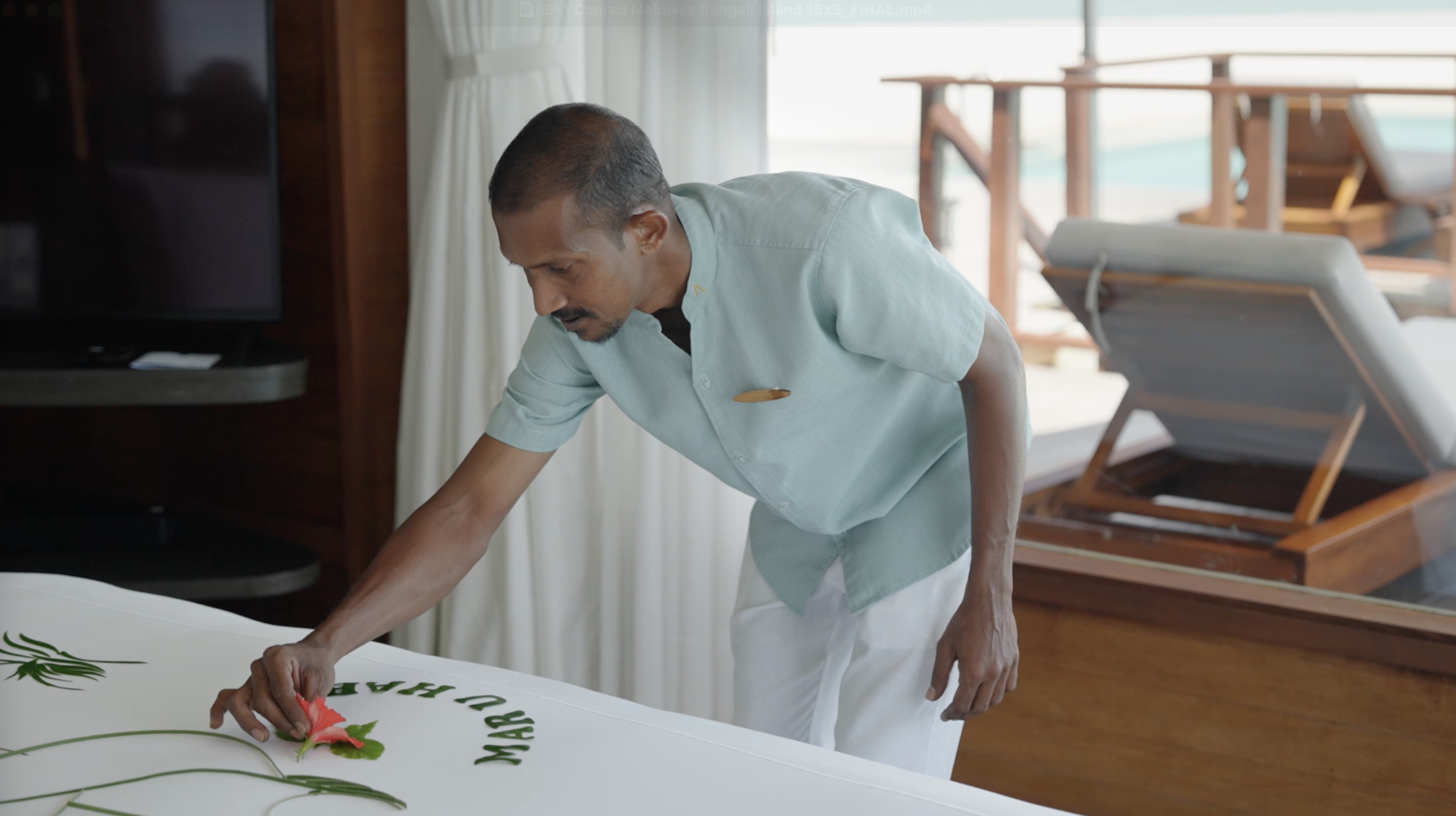 Conrad Maldives Rangali Island Team Member placing decorative flower petals on a guest room bed