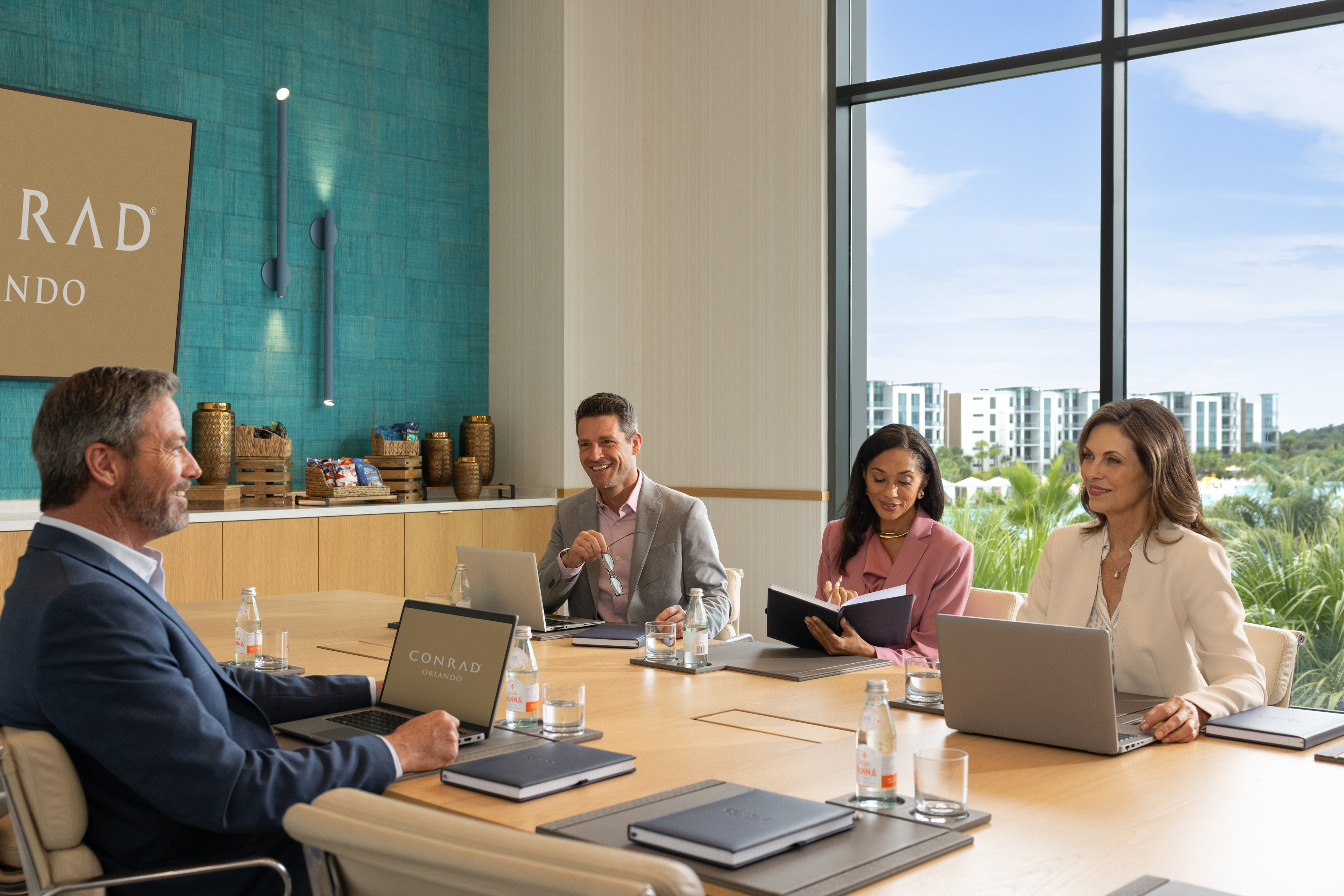 Four professionals in business attire having a meeting around a conference table with laptops and notebooks in the Lotus Boardroom at Conrad Orlando.