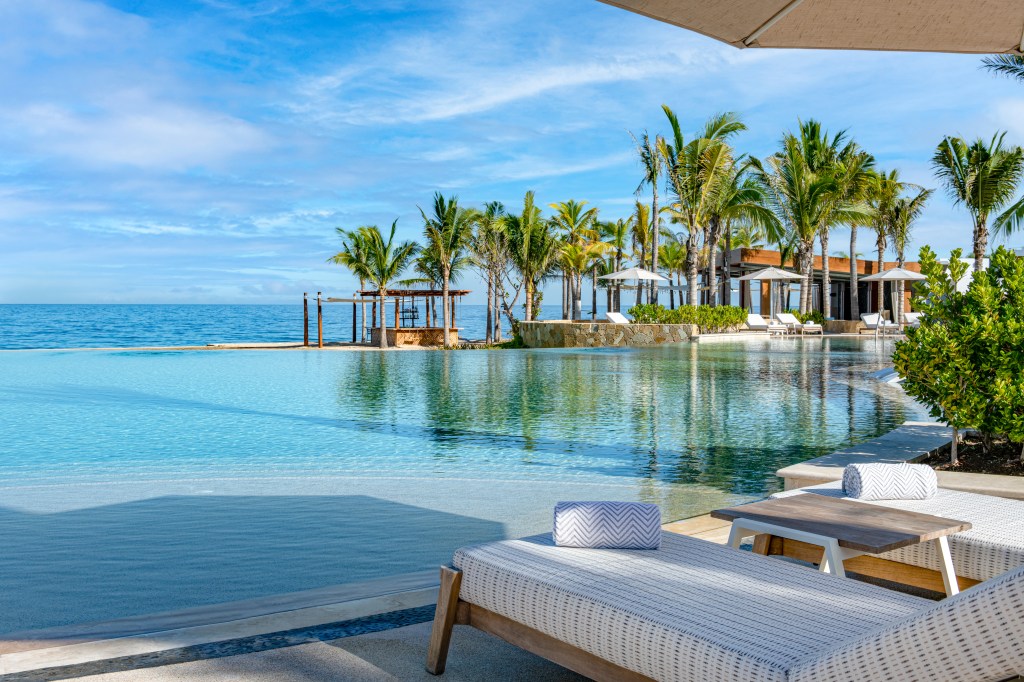 Infinity pool at Conrad Punta de Mita overlooking the ocean with palm trees, lounge chairs, and umbrellas.