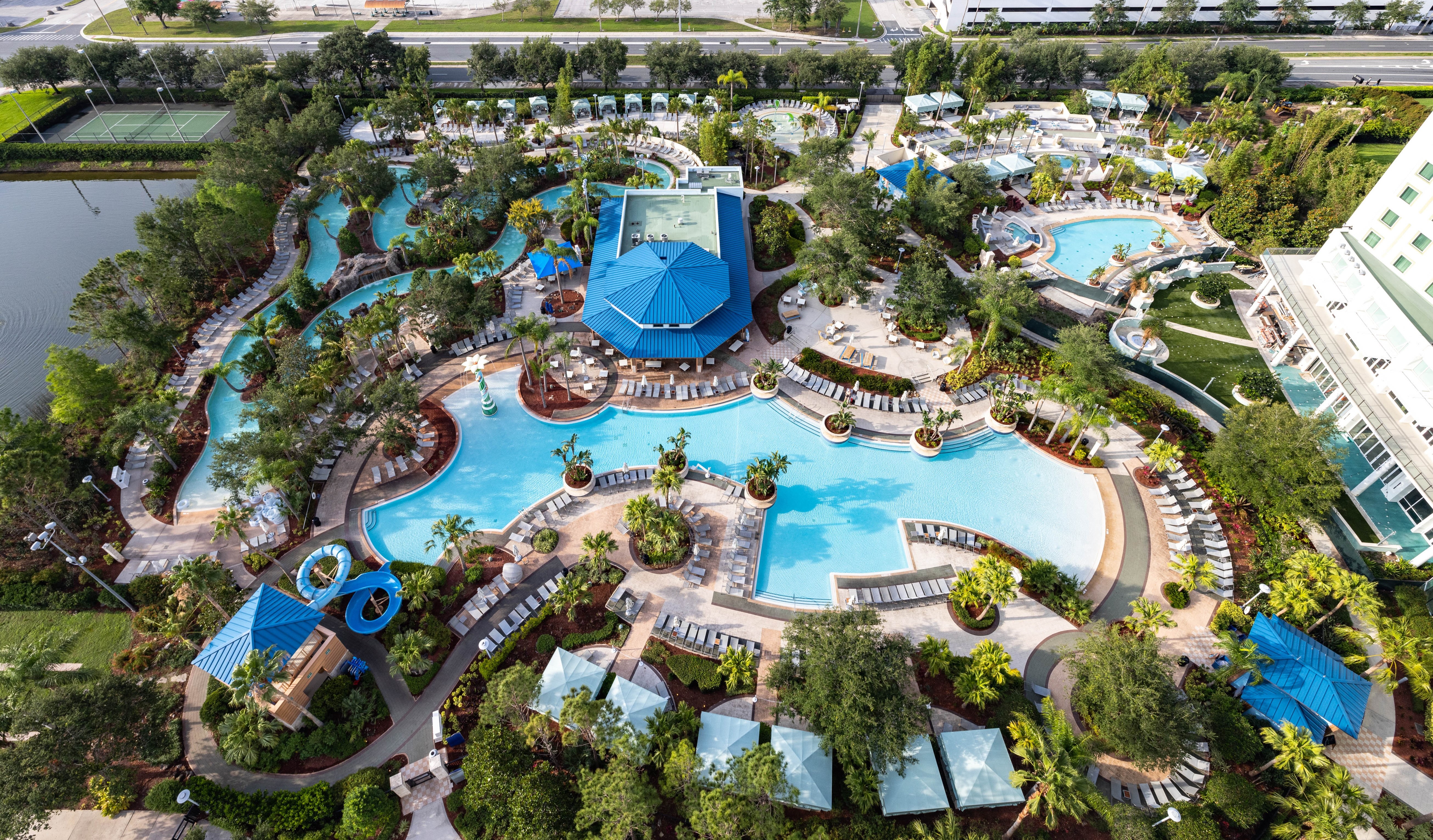 Hilton Orlando - Pool Aerial view of a large resort pool area with multiple swimming pools, water slides, lounge chairs, cabanas, and surrounding greenery.