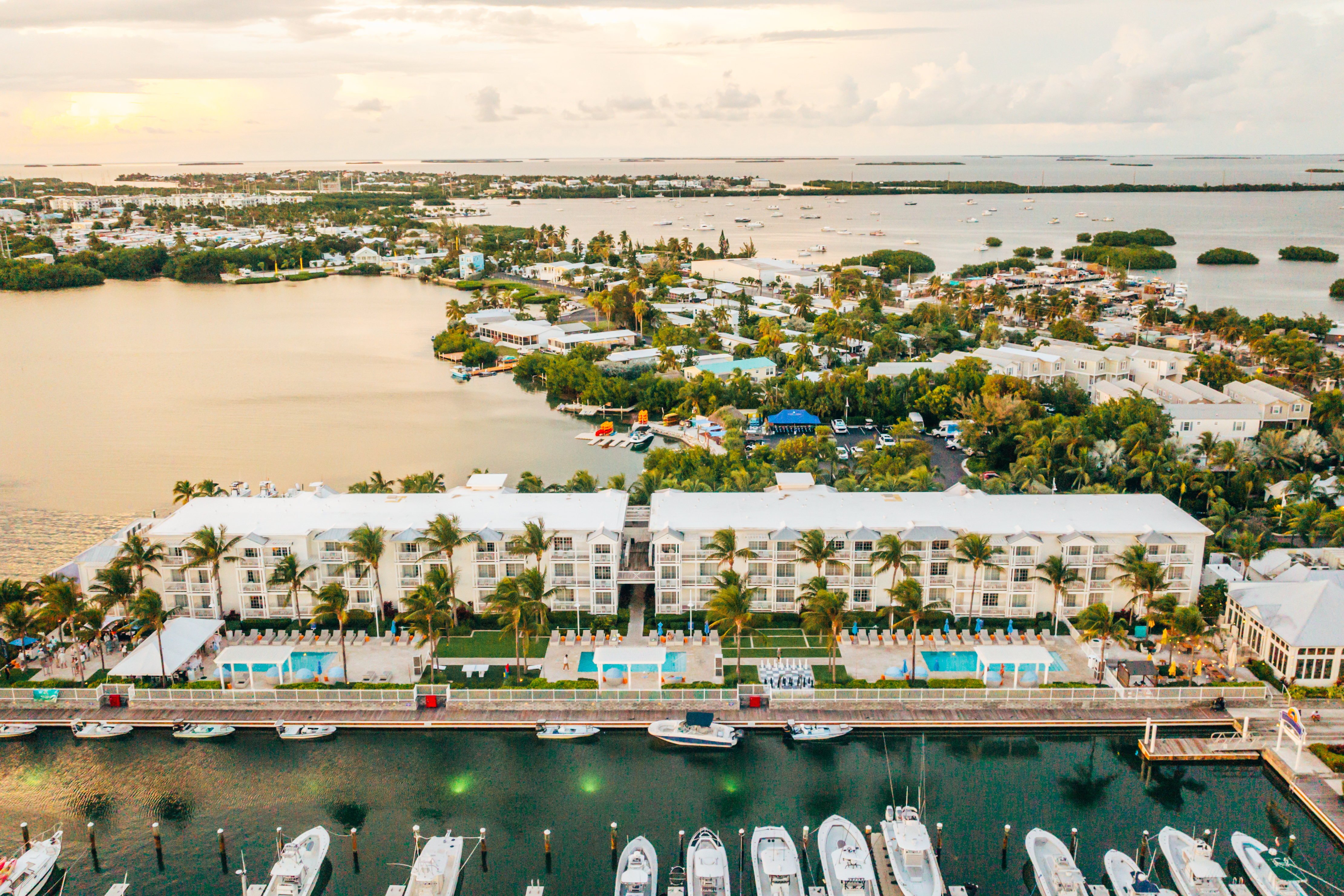 Aerial view of a waterfront Hilton Key West Resort Marina with two large buildings, swimming pools, palm trees, and boats docked along the marina.