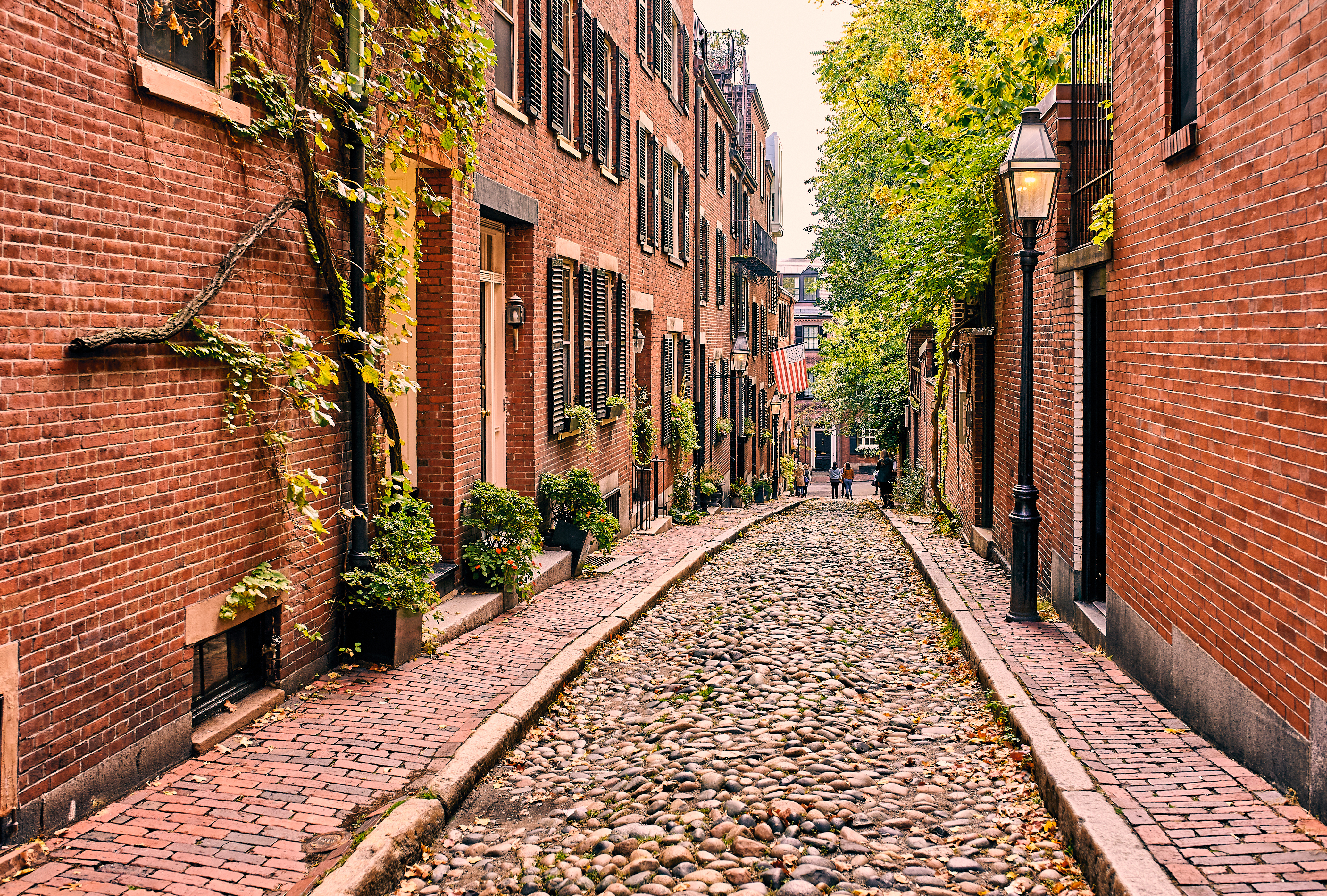 Narrow cobblestone street lined with red brick buildings and greenery in Beacon Hill Neighborhood in Boston, Massachusetts - Photo Credit: haveseen/Shutterstock