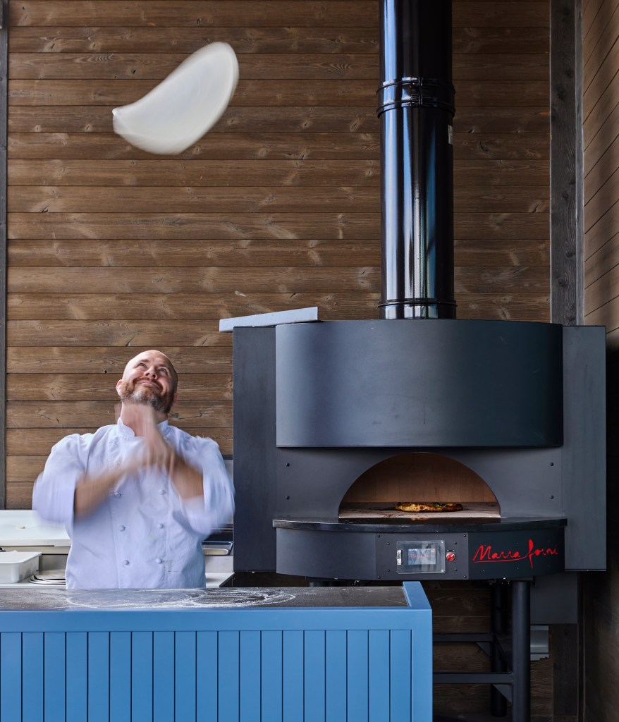 Chef tossing pizza dough in front of a wood-fired pizza oven at Canopy Deer Valley.