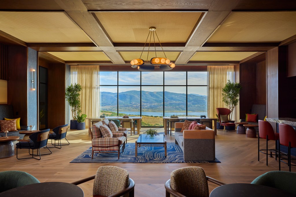 Spacious modern lounge with large windows showcasing a mountain and lake view, featuring comfortable seating and warm wooden accents at Canopy Deer Valley.