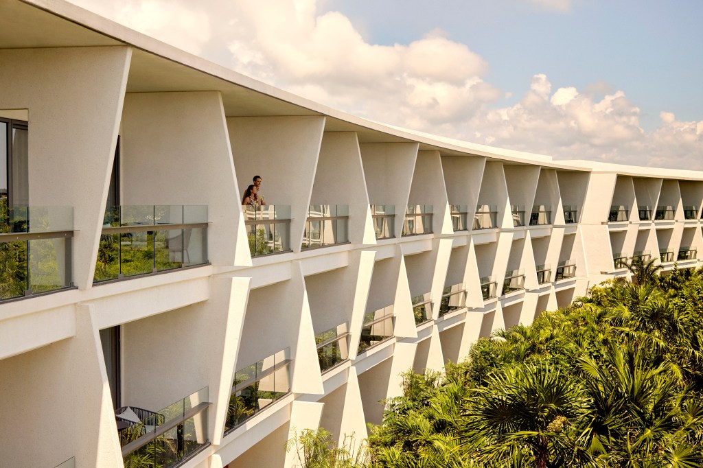 Modern white building with angled balconies overlooking lush green trees at Conrad Tulum Riviera Maya.